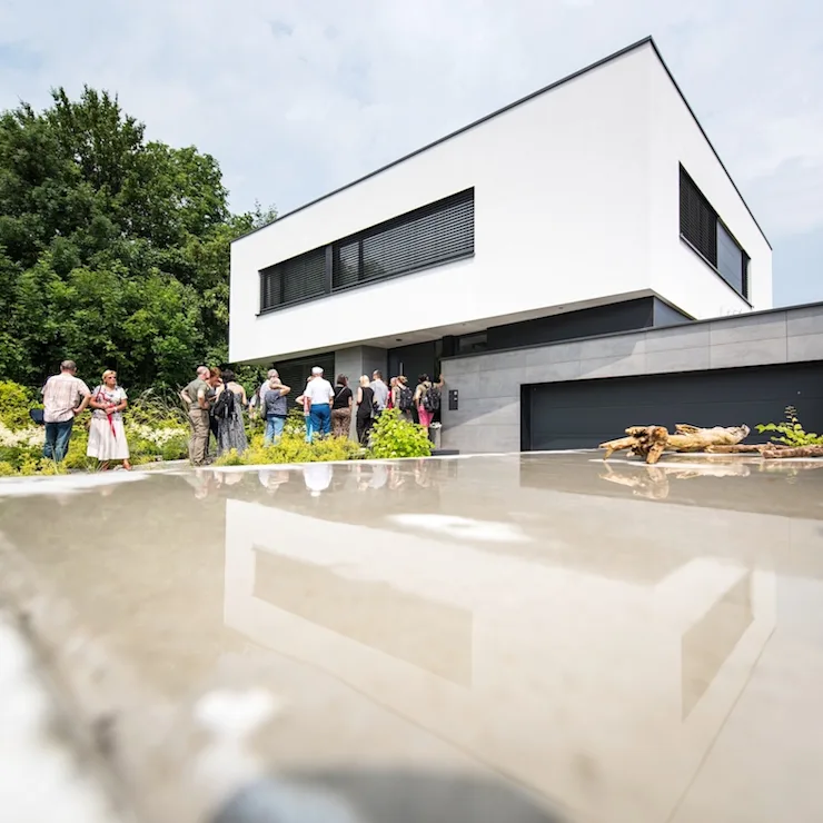 Mehrere Personen stehen vor einem modernen, weißen Wohnhaus mit flachem Dach und großem Garagentor.