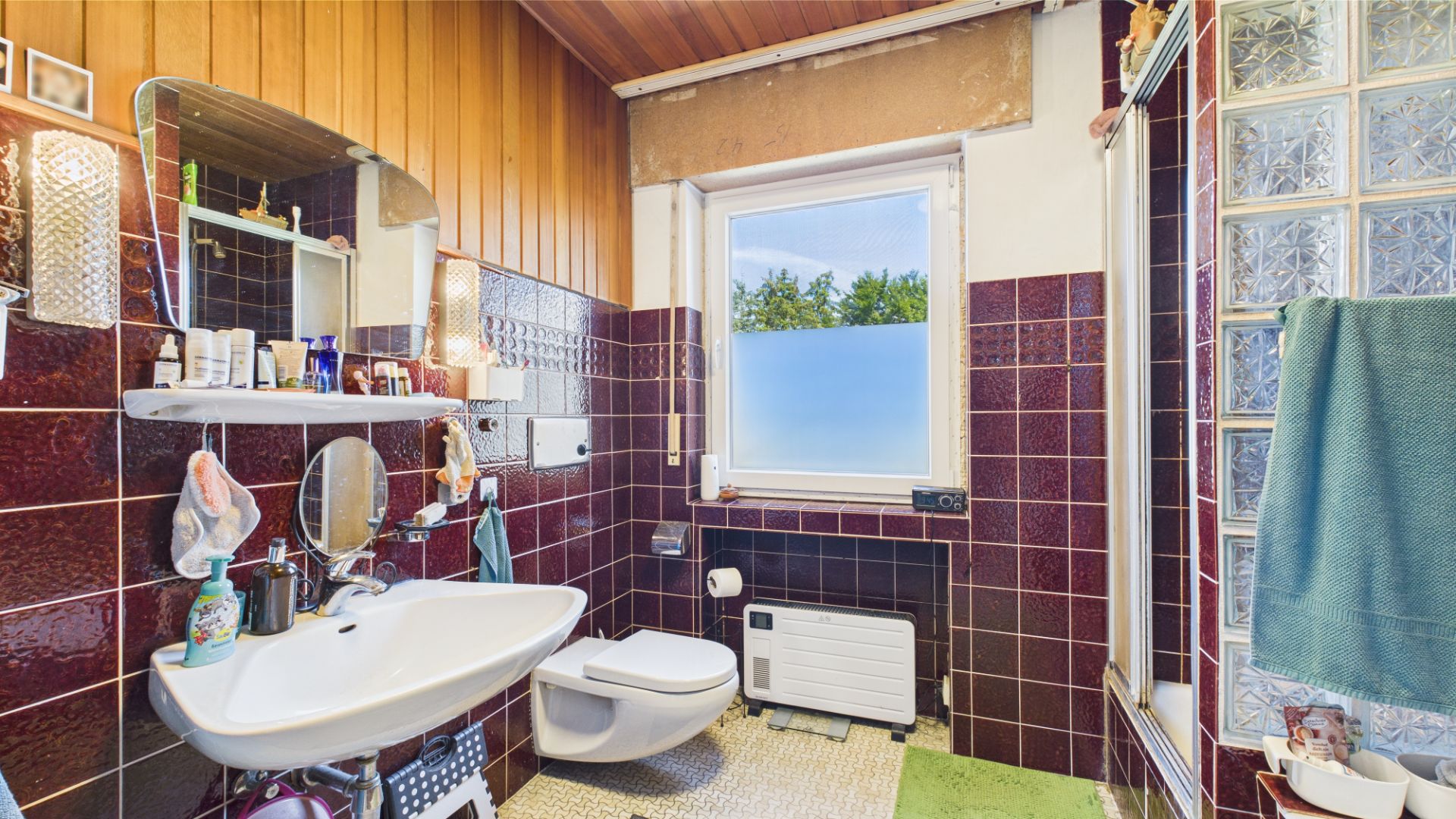 Badezimmer mit braunen Fliesen, WC, Waschbecken, Fenster und Dusche.