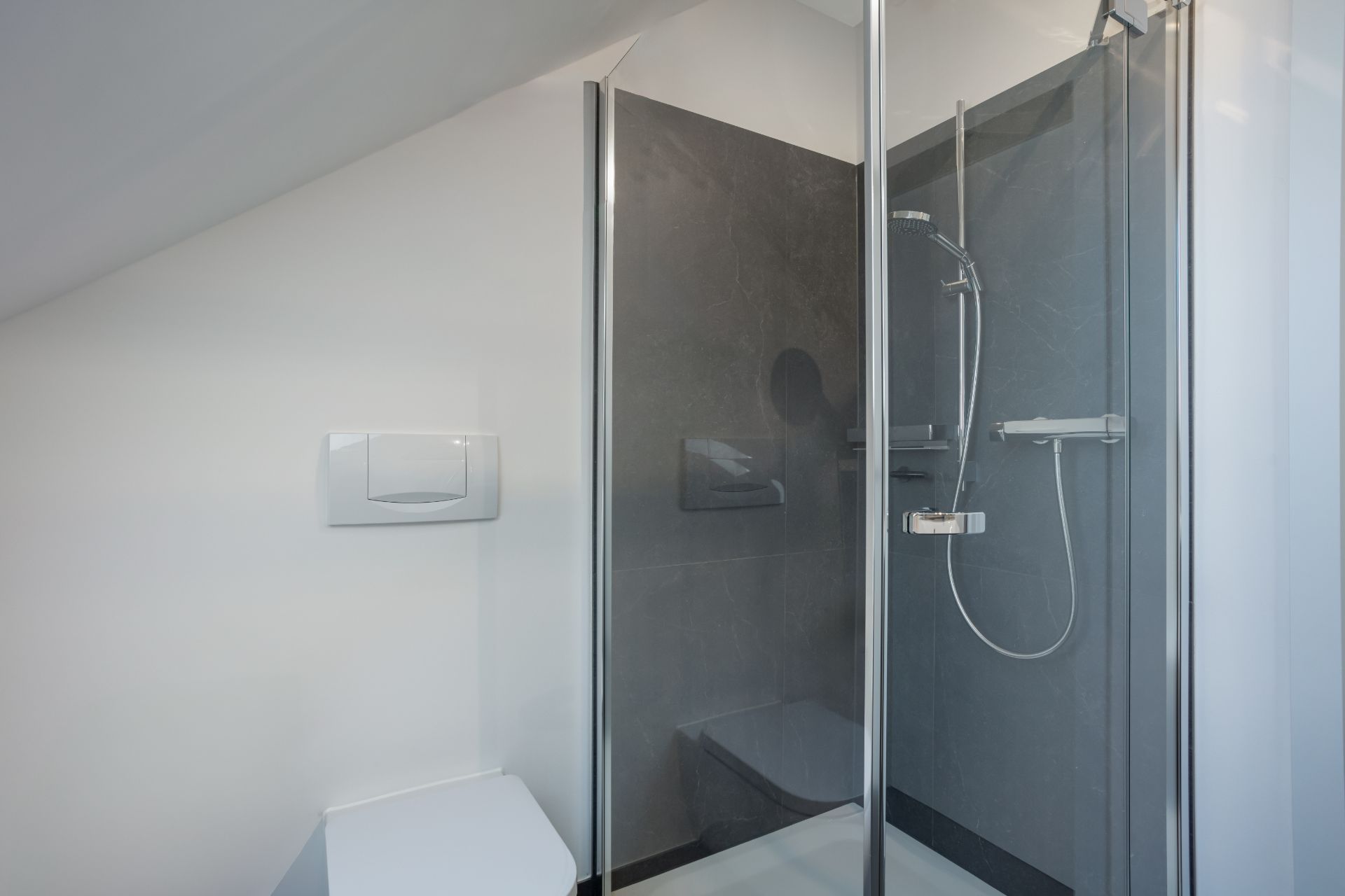 Modernes Badezimmer mit Dusche und Wandtoilette unter einer Dachschräge.