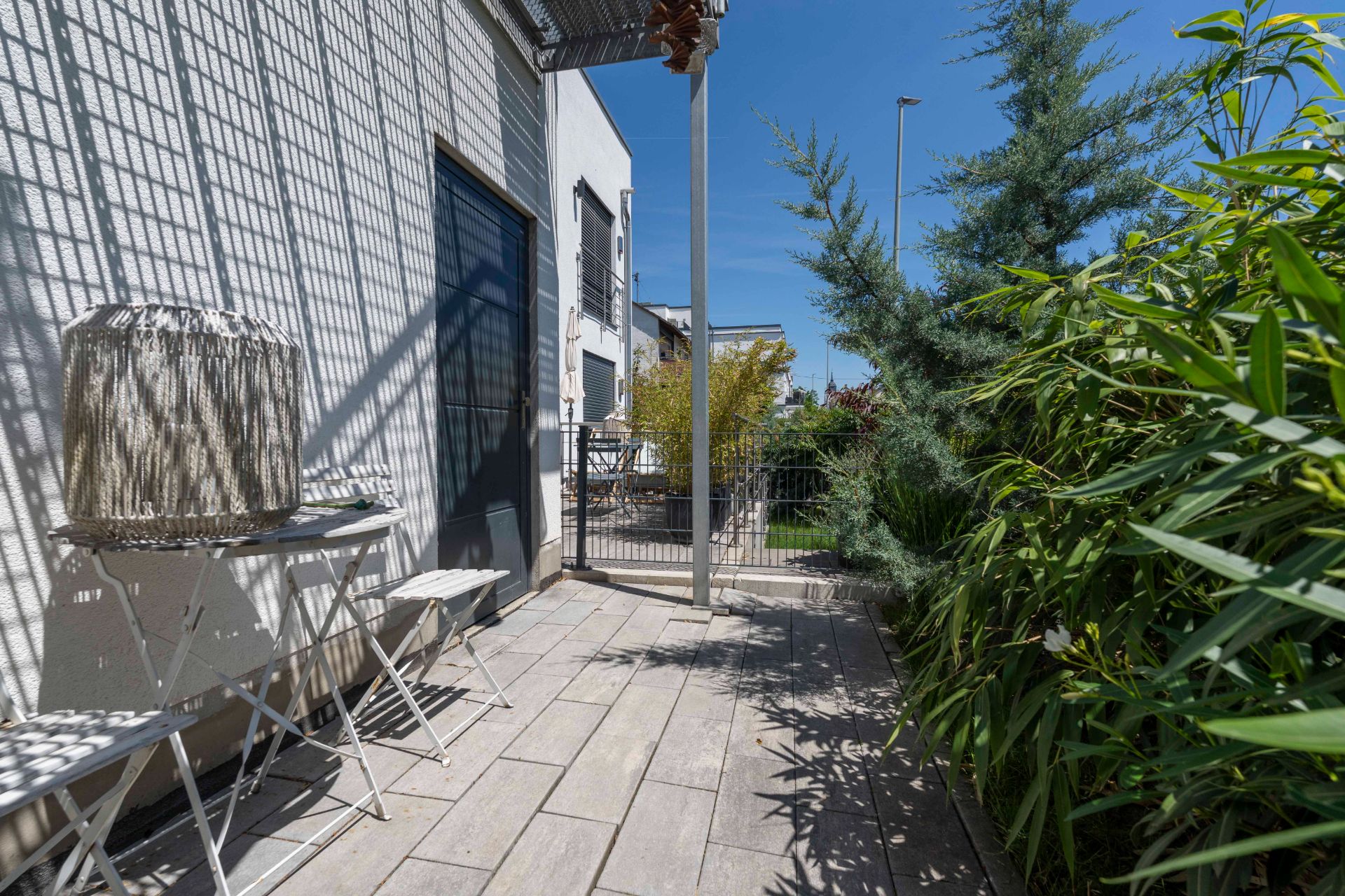 Kleine Terrasse mit Tisch, Stühlen und Pflanzen neben einem Wohnhaus.