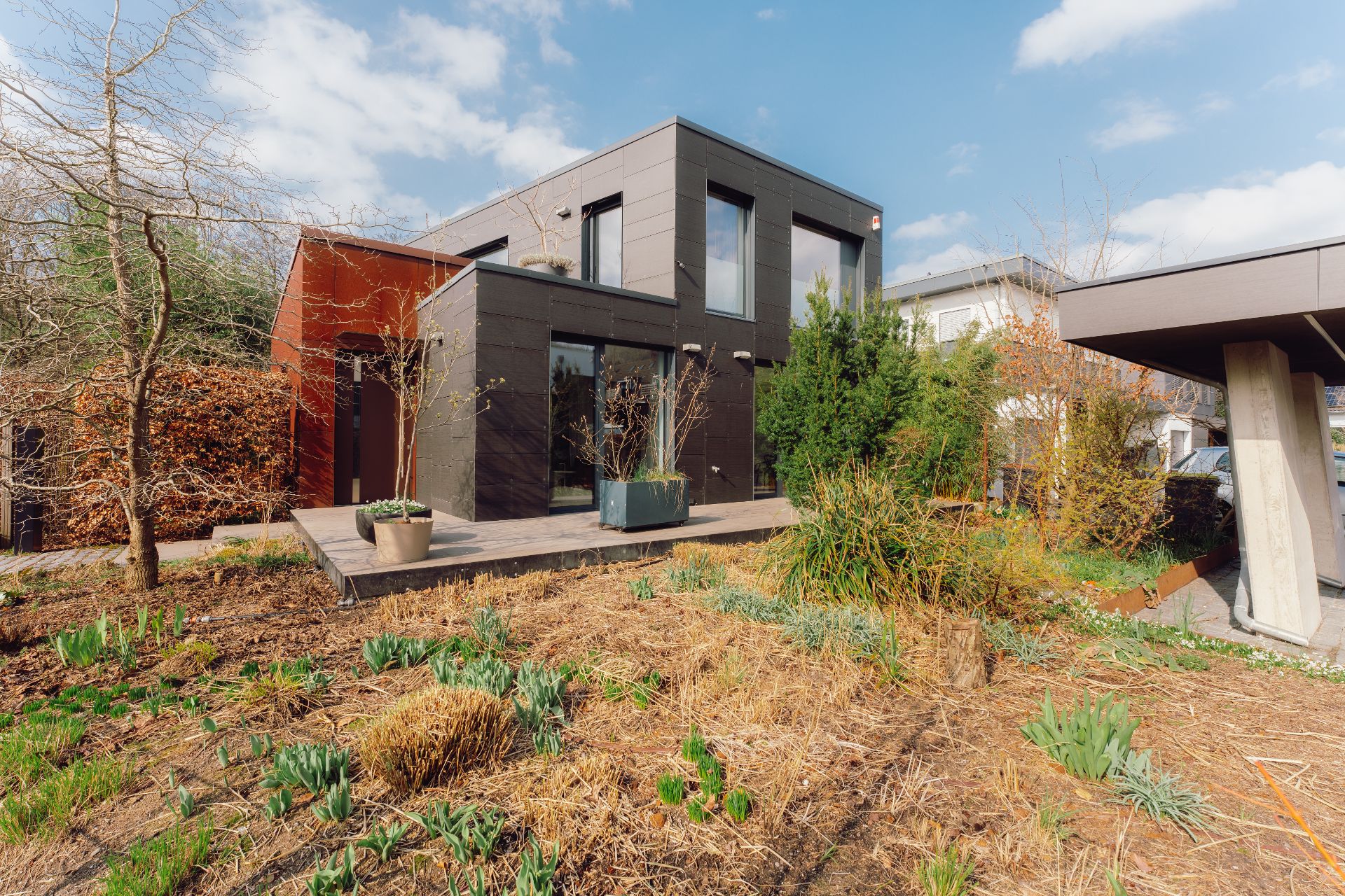 Modernes Wohnhaus mit großem Garten und Terrasse, Pflanzen und Bäumen im Vordergrund.