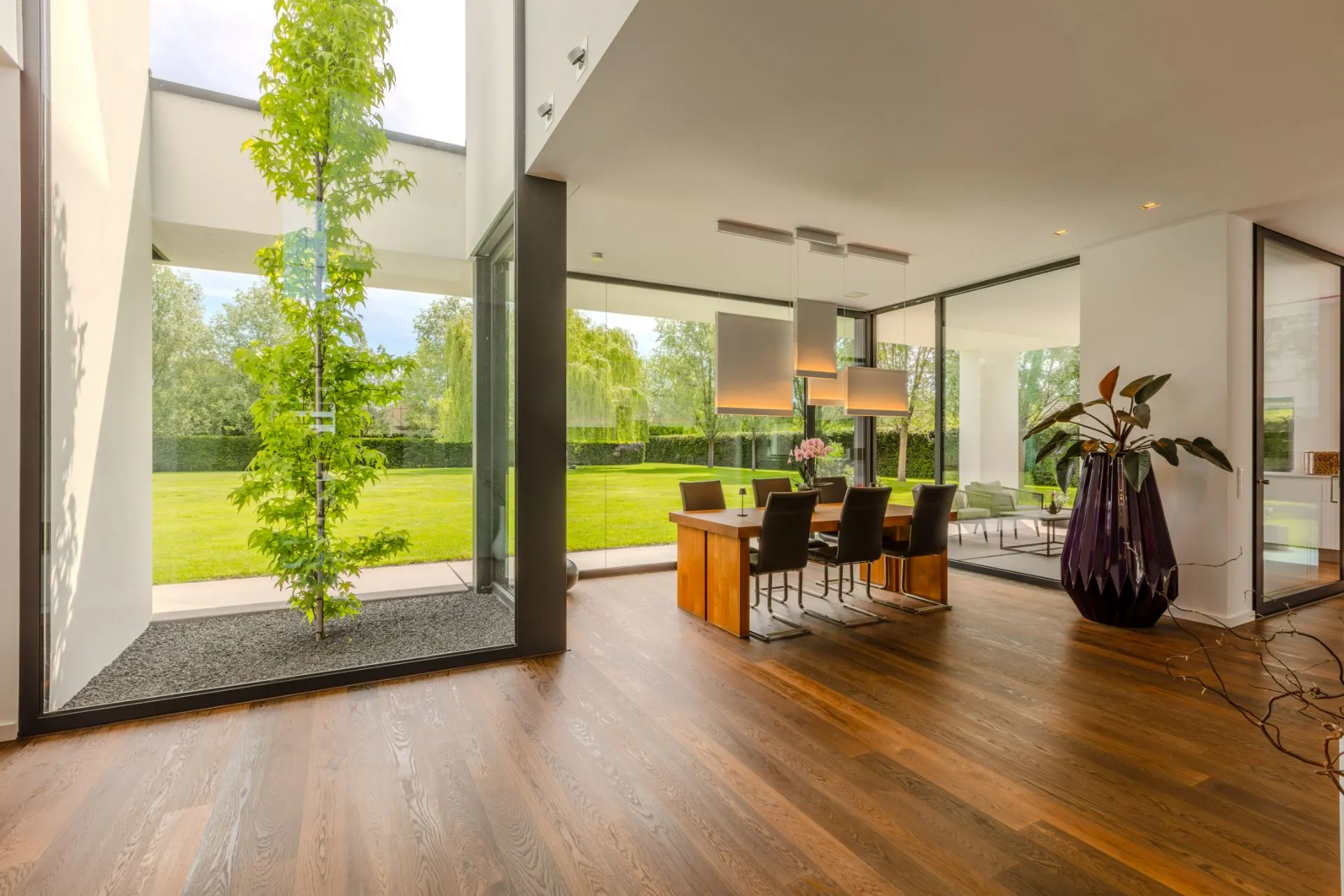 Modernes Esszimmer mit Holzboden, großen Fenstern und Blick auf einen grünen Garten.