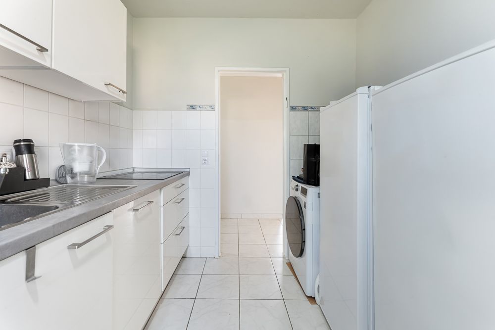 Helle Küche mit weißen Schränken, Waschmaschine und großem Kühlschrank.