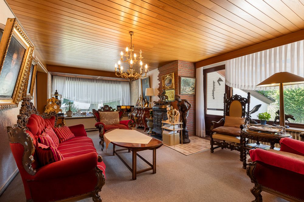 Wohnzimmer mit roten Polstermöbeln, Holzdecke, Kronleuchter und großen Fenstern.