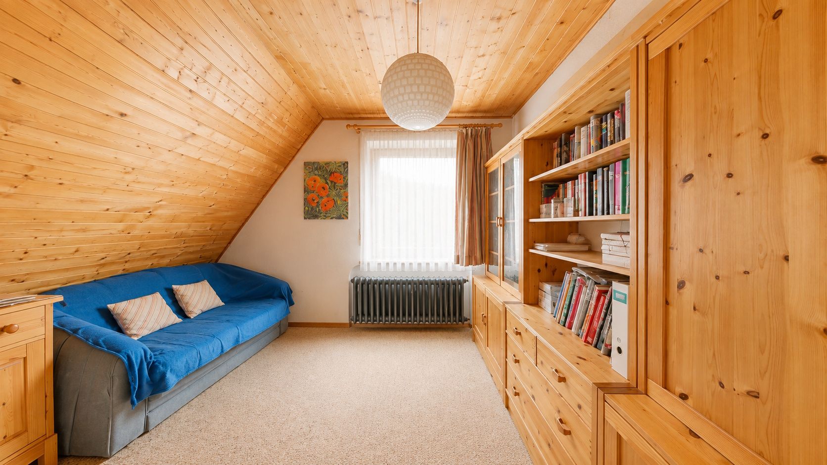 Gemütliches Zimmer mit Holzdecke, blauem Sofa, Bücherregal und Fenster mit Vorhängen.