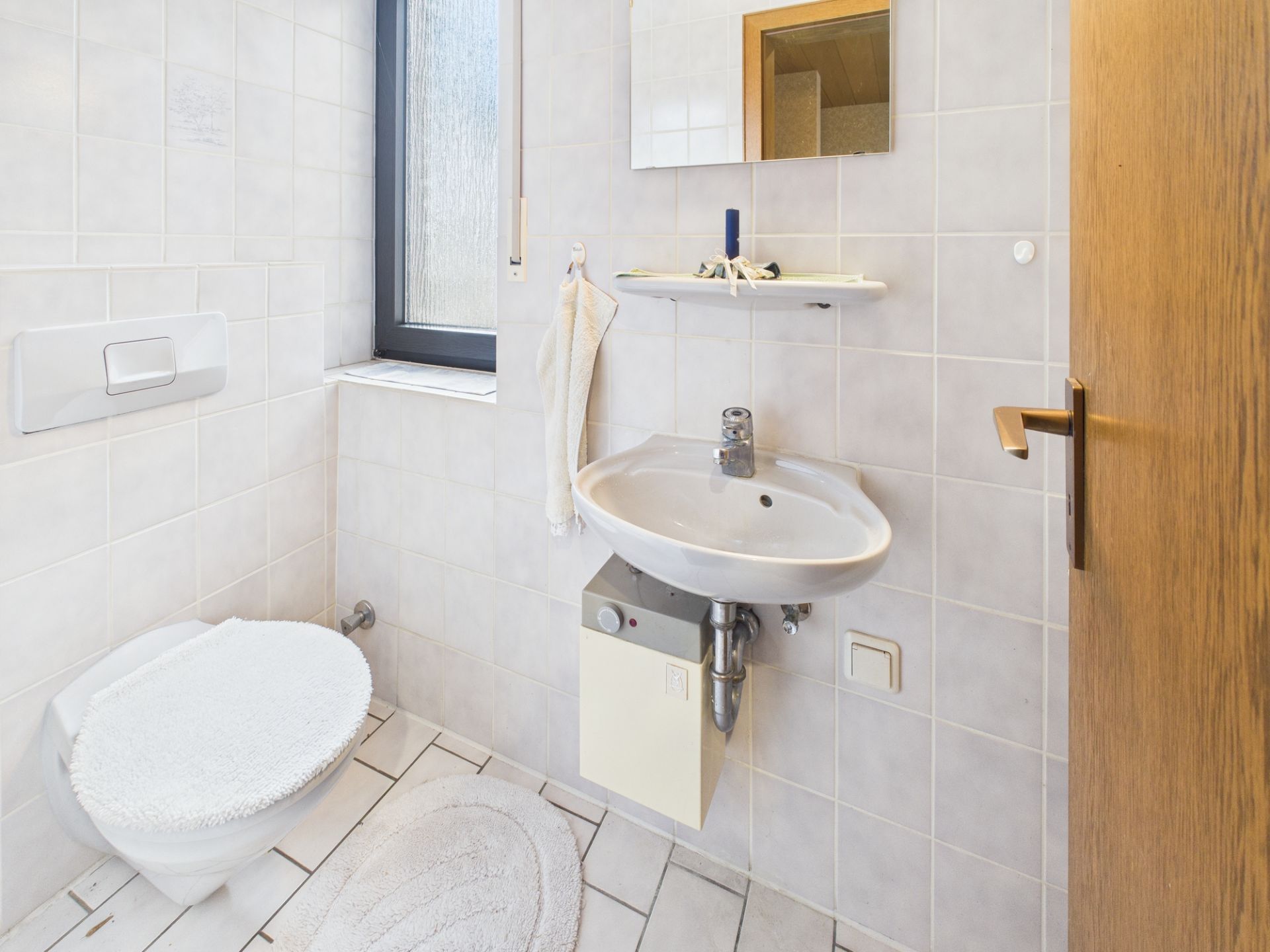 Helles Badezimmer mit Toilette, Waschbecken, Spiegel und Fenster.