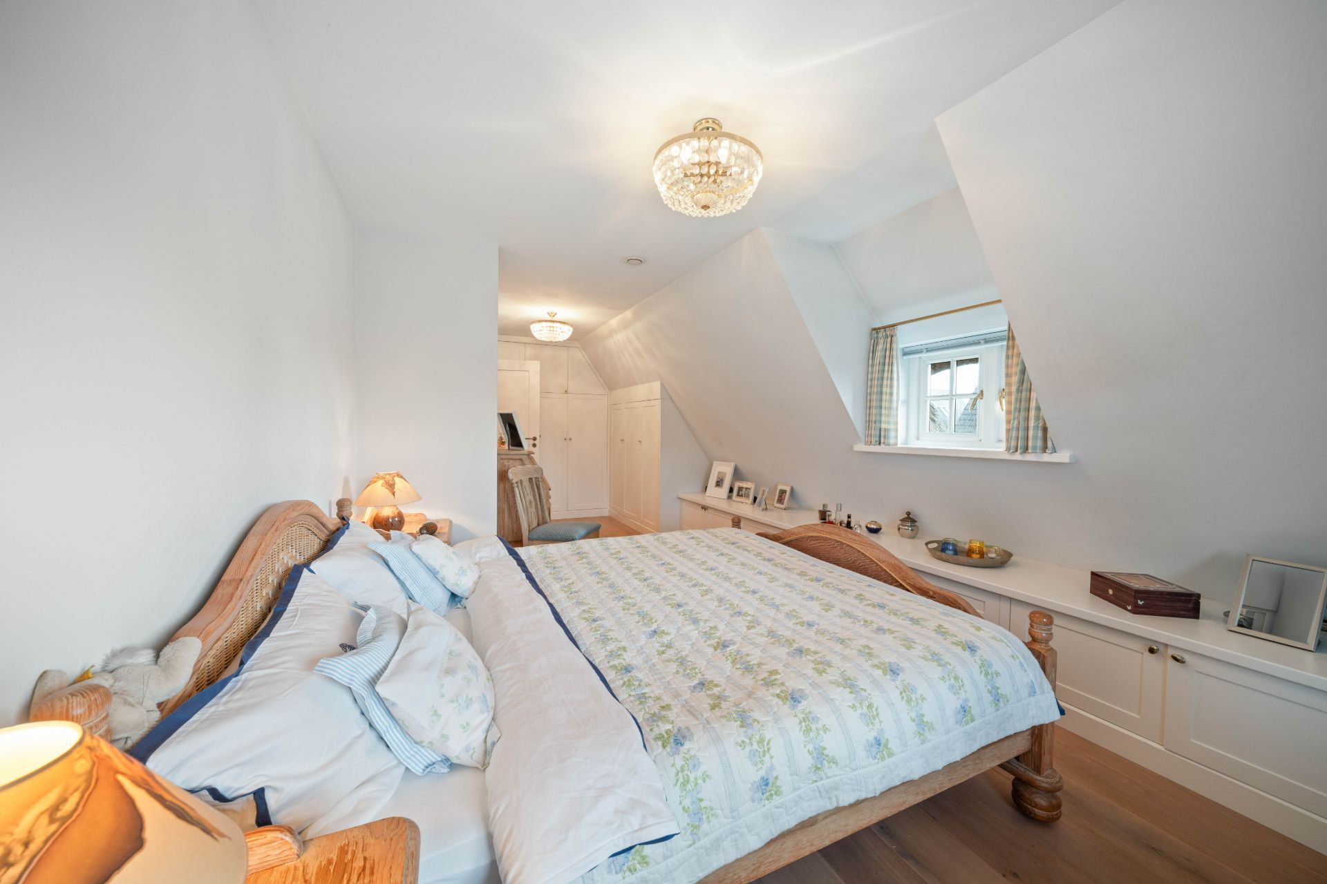 Helles Schlafzimmer mit großem Holzbett, Fenster und Einbauschränken unter der Dachschräge.