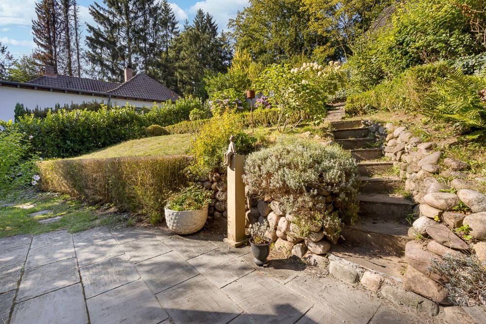 Gepflegter Garten mit Steintreppe, Pflanzen und Terrasse, im Hintergrund ein Wohnhaus.