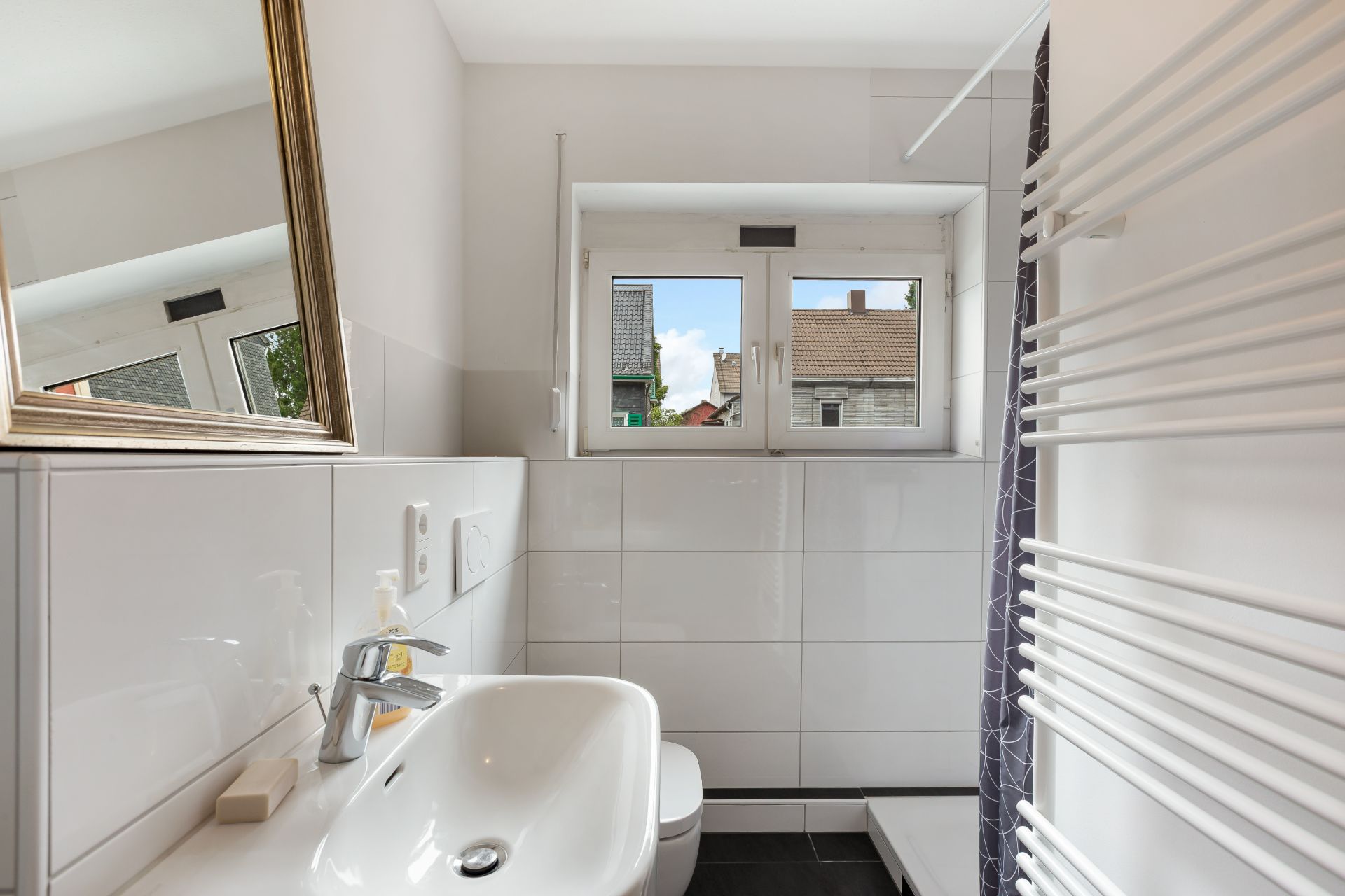 Modernes Badezimmer mit Waschbecken, Spiegel, Fenster und Handtuchheizkörper.