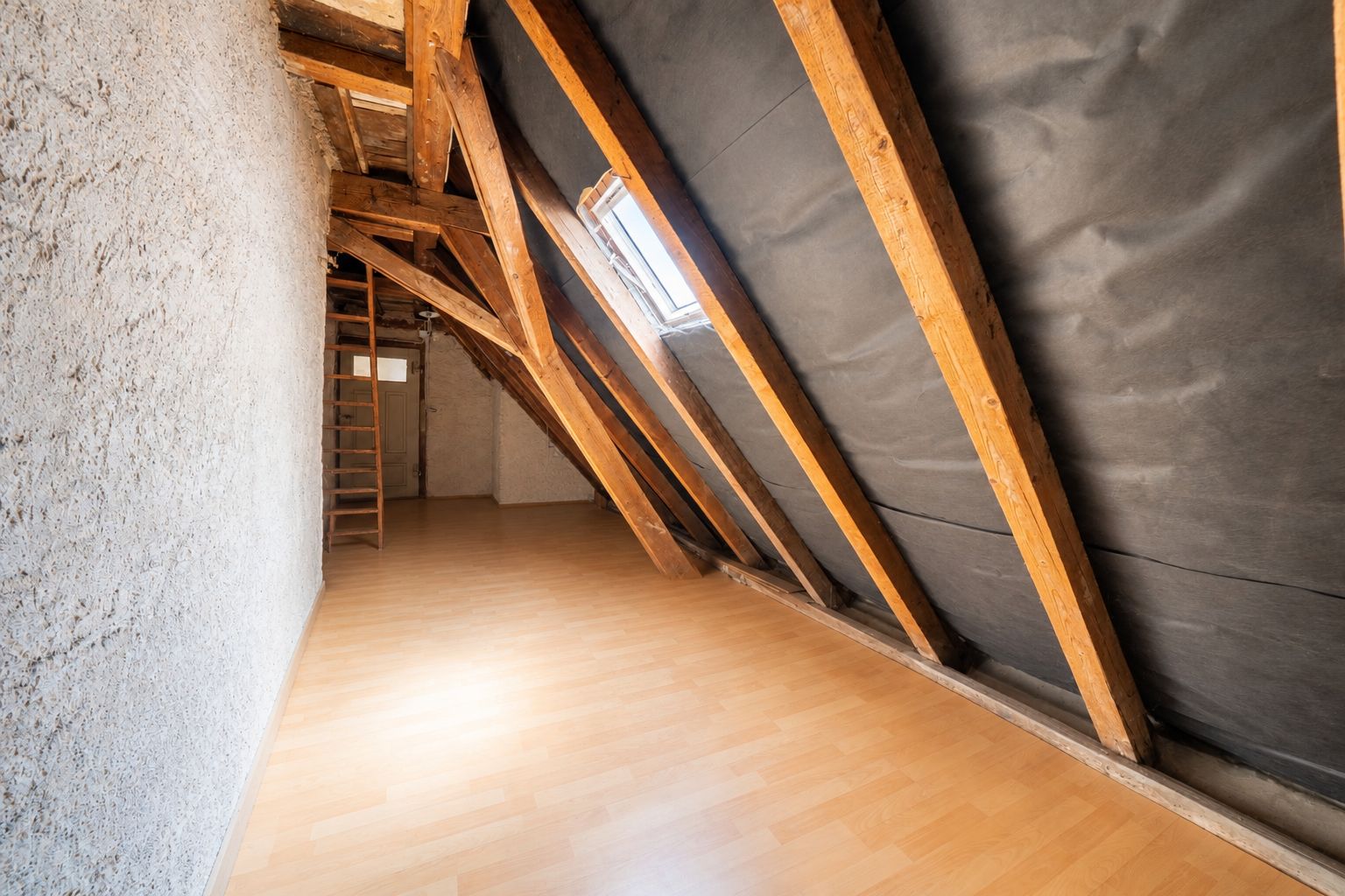 Ausgebauter Dachboden mit Holzträgern, Laminatboden und Dachfenster.