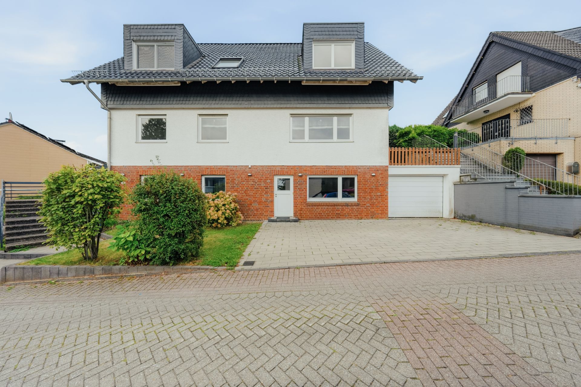 Zweistöckiges Wohnhaus mit rotem Klinkersockel, Garage und kleinem Vorgarten.