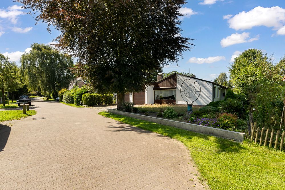 Wohnstraße mit Bäumen links und einem Haus mit Garten rechts.
