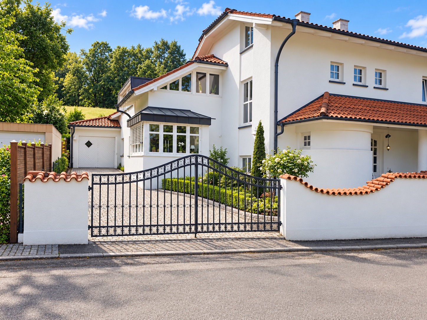 Weißes Wohnhaus mit rotem Dach, Einfahrtstor und kleiner Garten vor dem Haus.