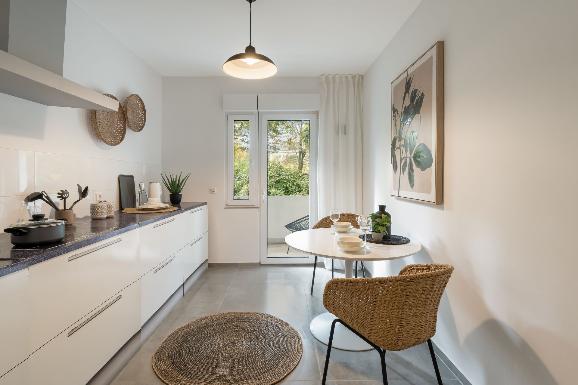 Moderne Küche mit Esstisch, zwei Stühlen und Zugang zu einem Balkon, dekoriert mit Naturmaterialien.