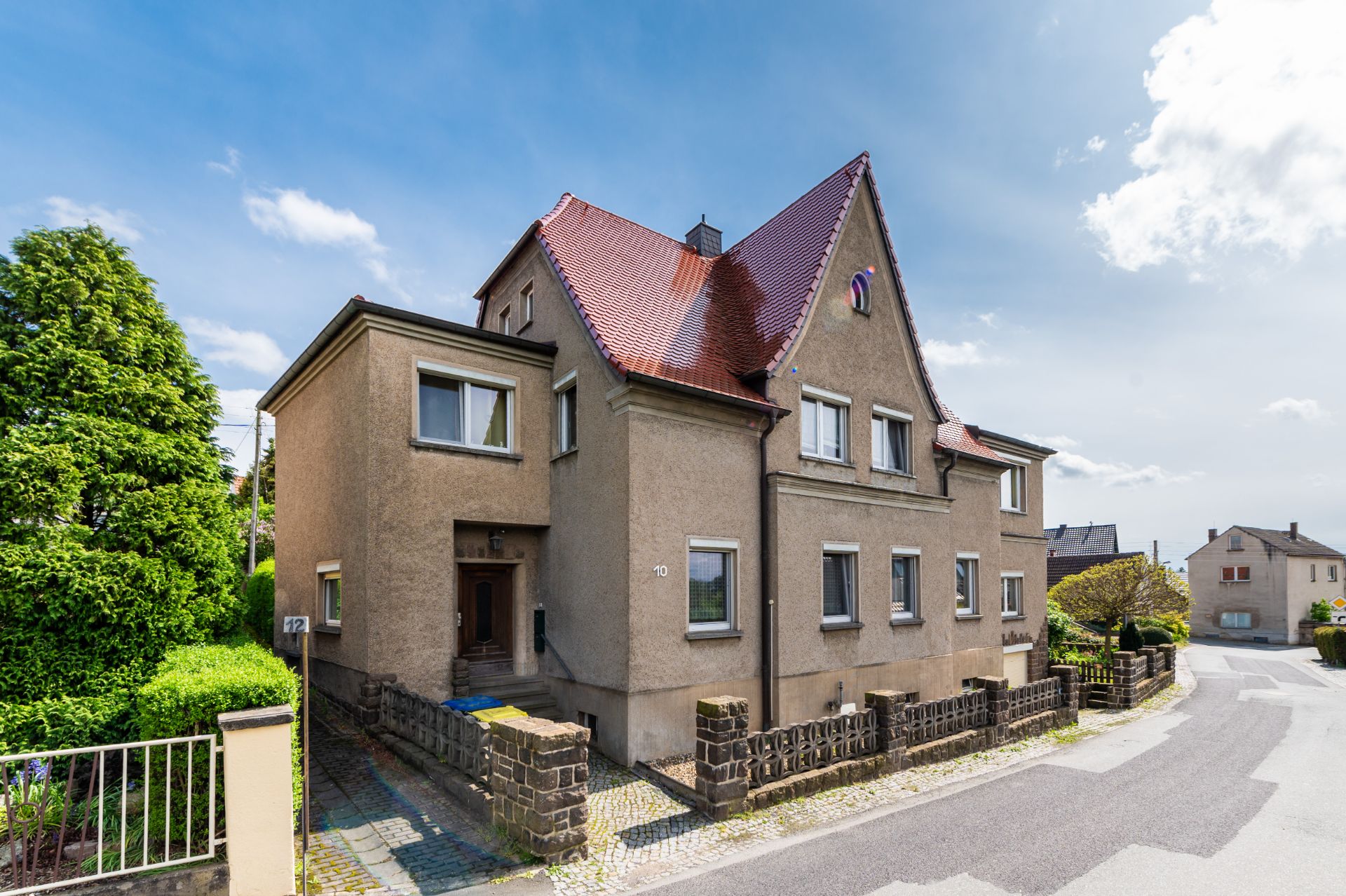 Zweistöckiges Wohnhaus mit rotem Satteldach und mehreren Fenstern an einer Straßenecke.