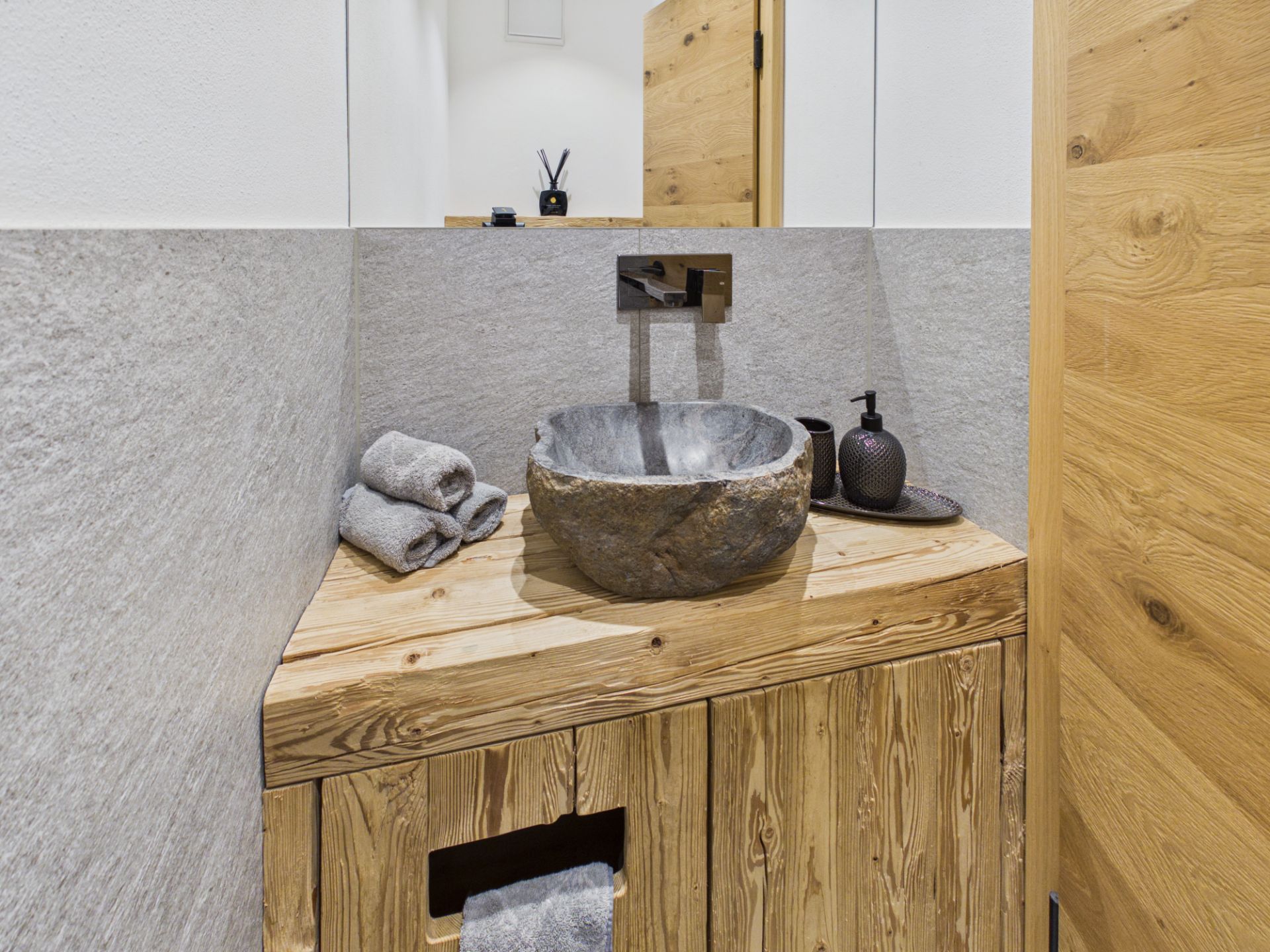 Kleines Badezimmer mit Waschbecken aus Stein auf hölzerner Arbeitsplatte, Handtücher und Seifenspender.