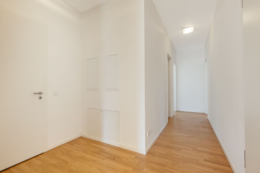 Heller Flur mit weißen Wänden und Holzboden in einer Wohnung.