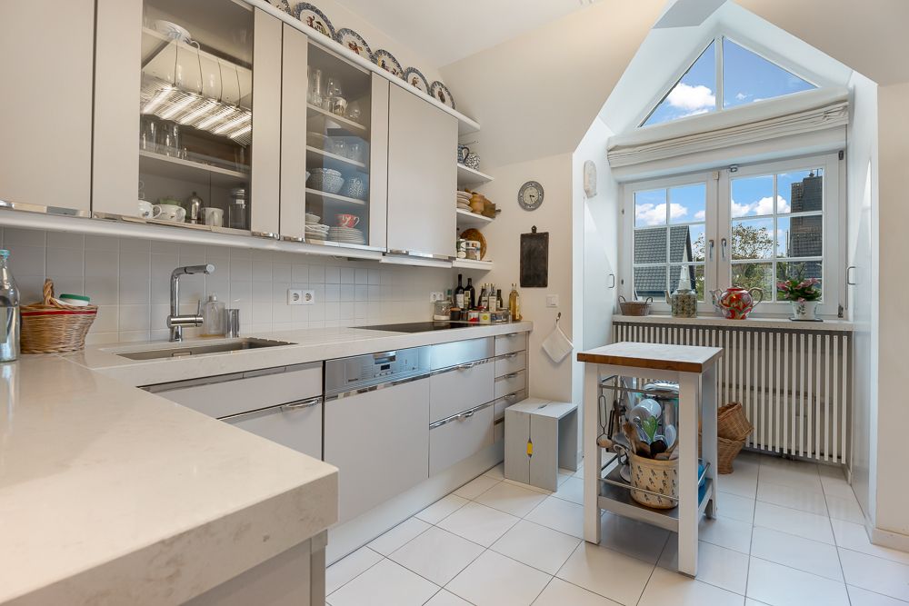 Moderne, helle Küche mit weißen Schränken, Kücheninsel und großem Fenster mit Blick nach draußen.
