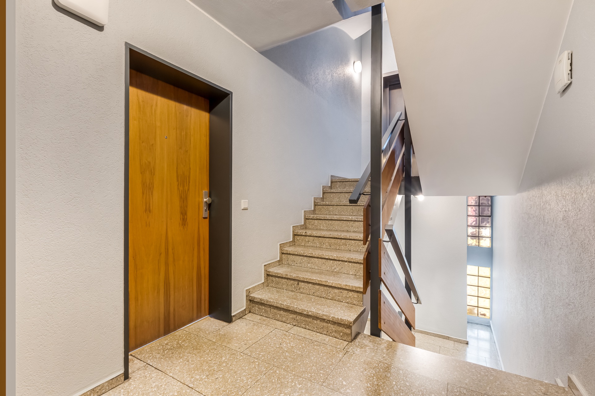 Treppenhaus mit brauner Wohnungstür und Treppen nach oben und unten.