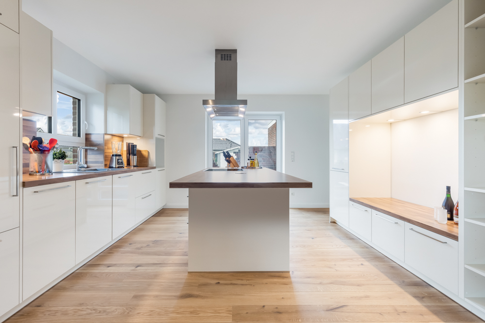 Moderne, helle Küche mit Kochinsel, weißen Schränken und Holzboden.
