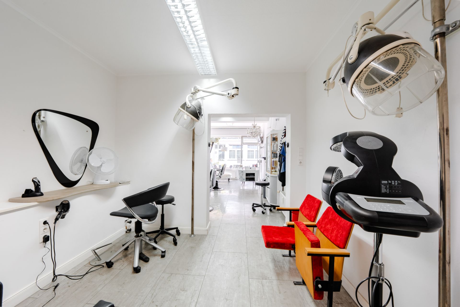 Heller Raum mit roten Stühlen, Friseurstühlen, Spiegeln und Haartrocknern an der Wand.