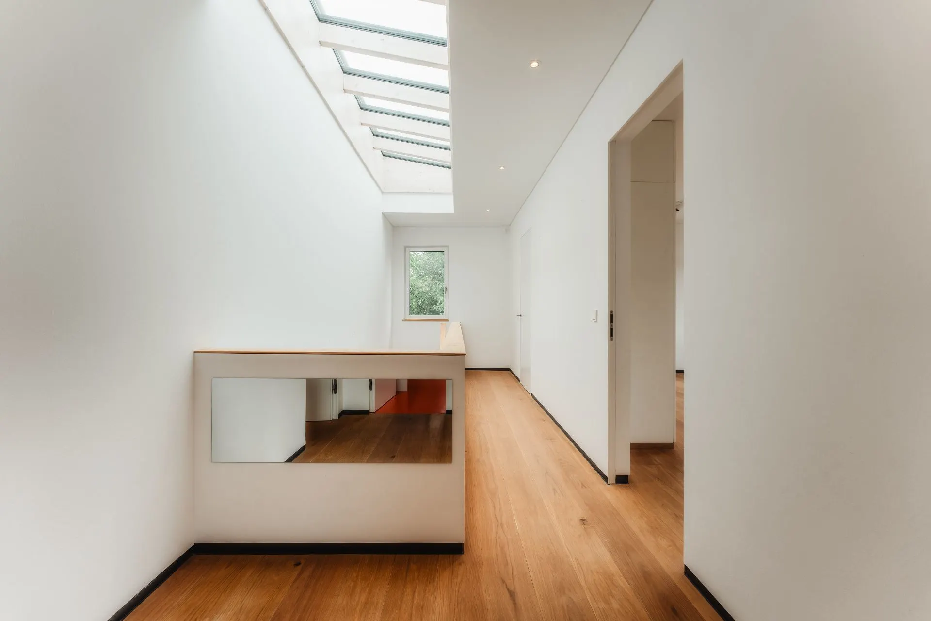 Heller Flur mit Holzfußboden, Oberlicht und Fenster, weiße Wände, Spiegel an der Wand.