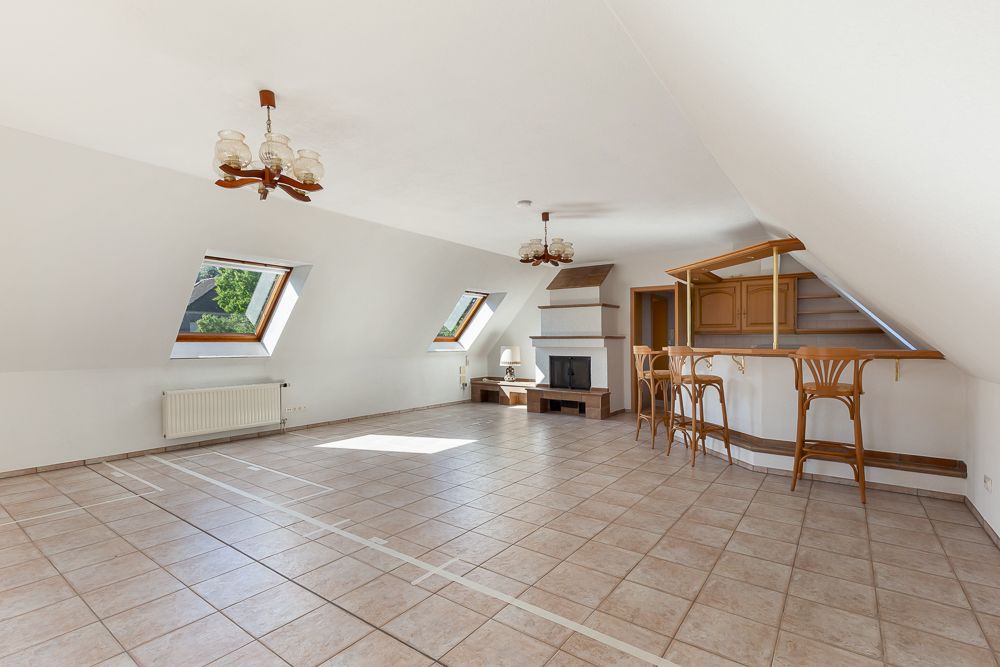 Heller Dachgeschossraum mit Fliesenboden, zwei Dachfenstern, Kamin und offener Küchenzeile mit Tresen.