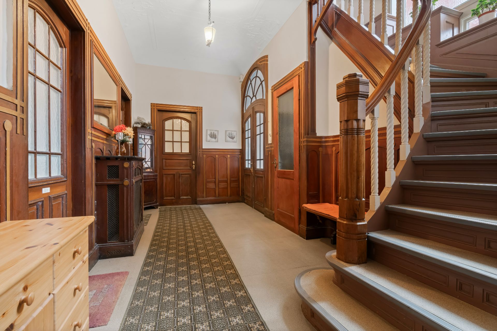 Heller Flur mit Holztreppe, Teppichläufer und Holztüren in einem Wohnhaus.