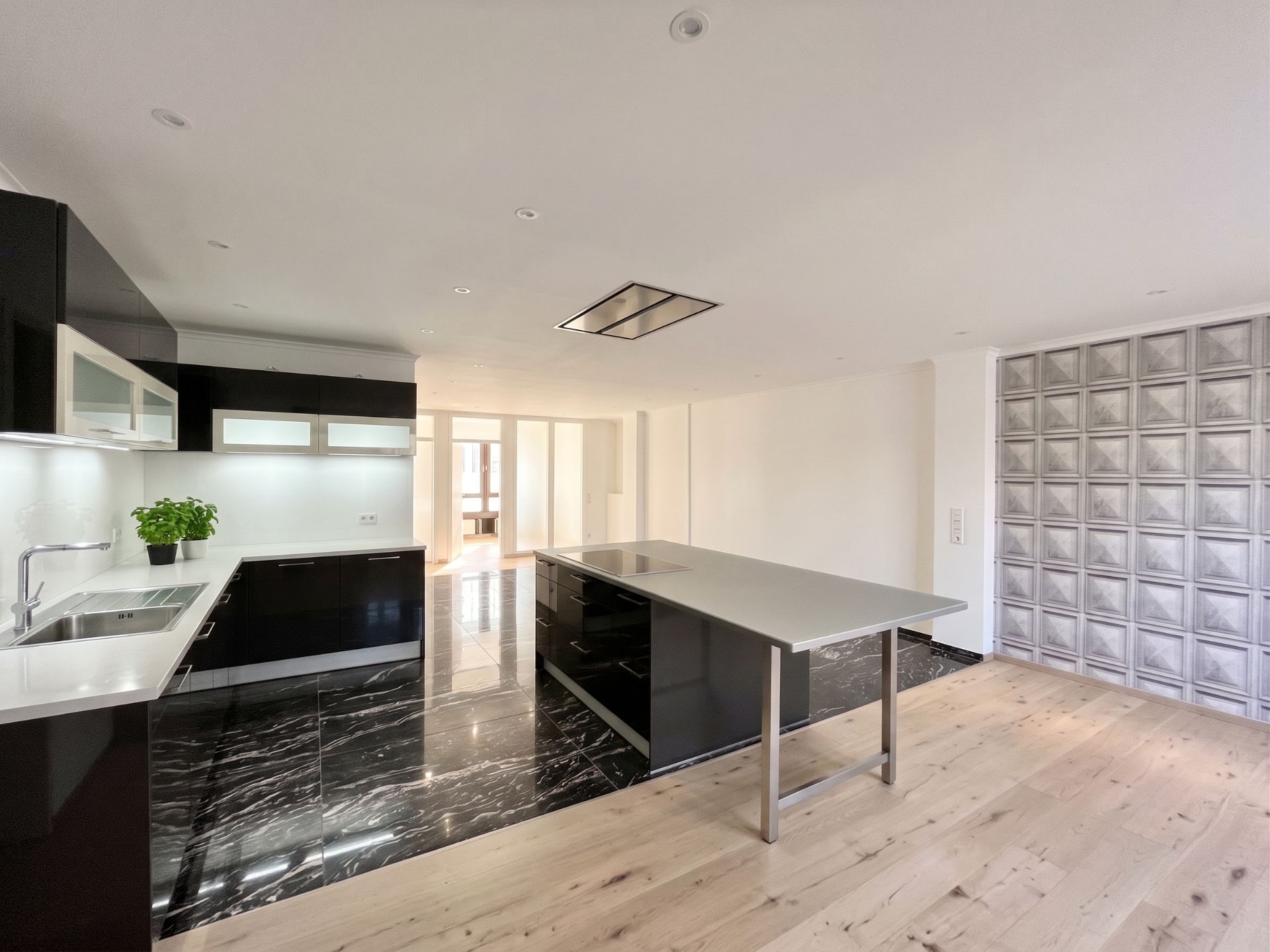 Moderne Küche mit Kochinsel, schwarzen Schränken und Marmor- sowie Holzfußboden.