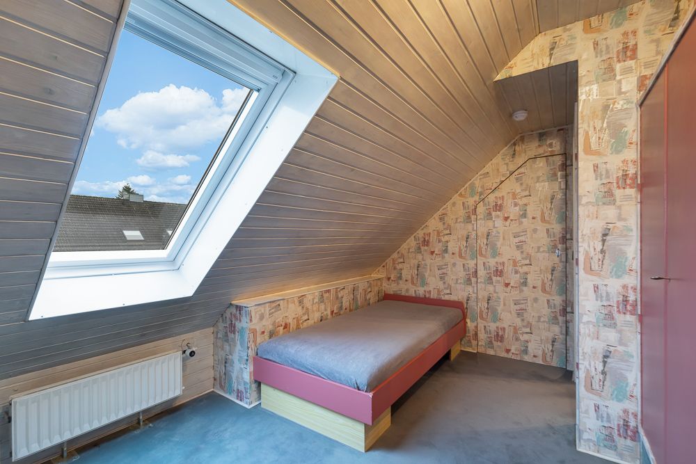 Kleines Dachzimmer mit Einzelbett, großem Dachfenster und gemusterter Tapete.