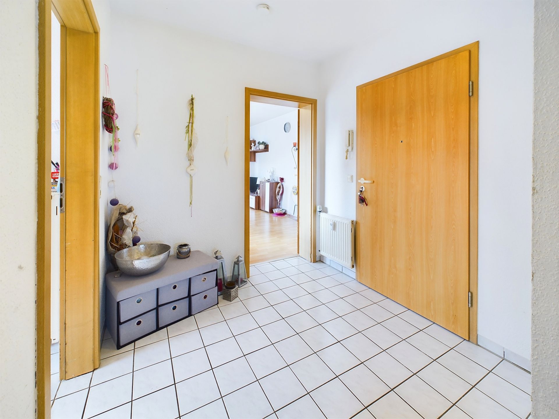 Heller Flur mit weißem Fliesenboden, Holztüren und kleiner Kommode an der Wand.