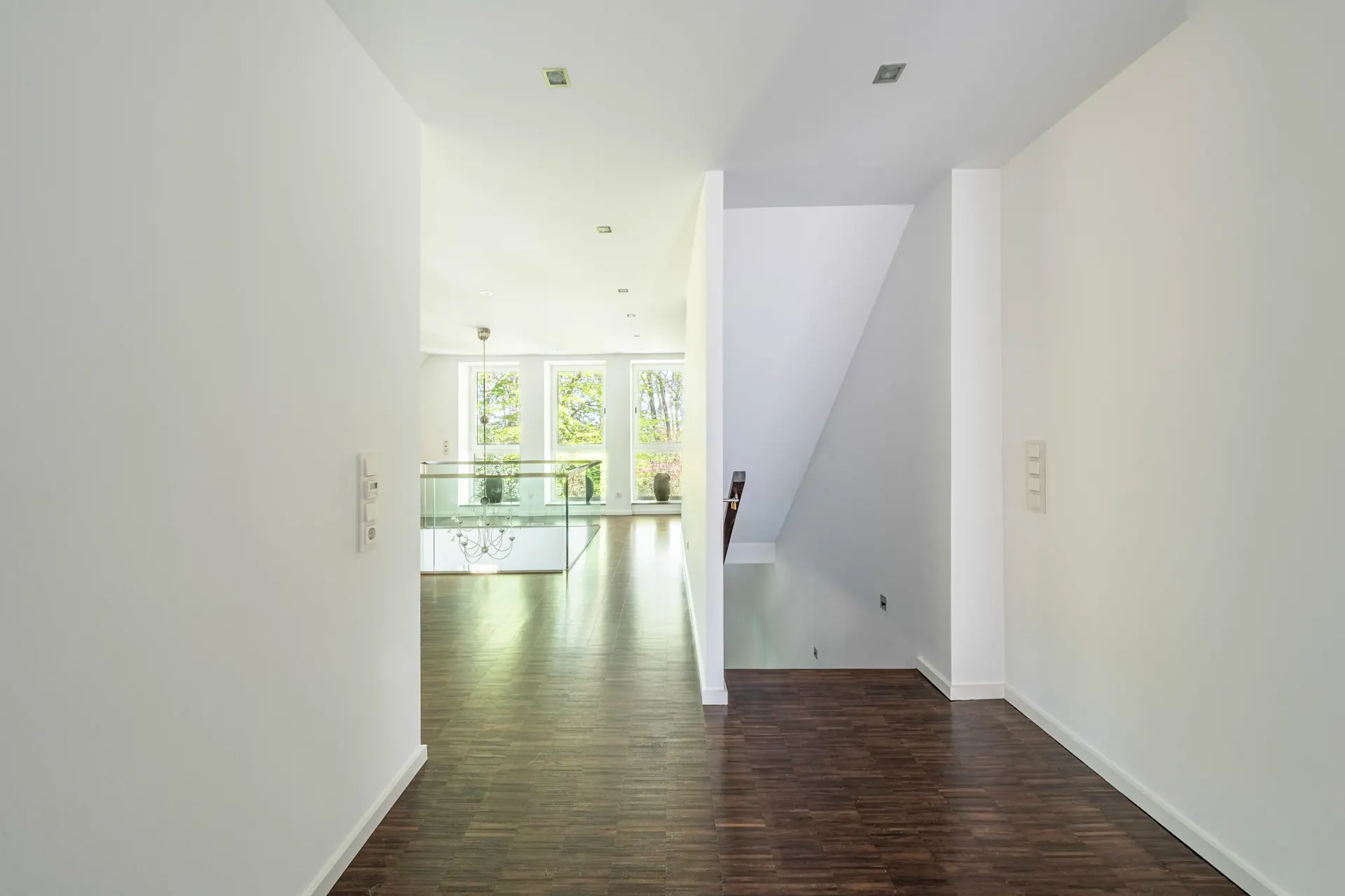 Heller Flur mit dunklem Holzboden, Treppe und großen Fenstern im Hintergrund.