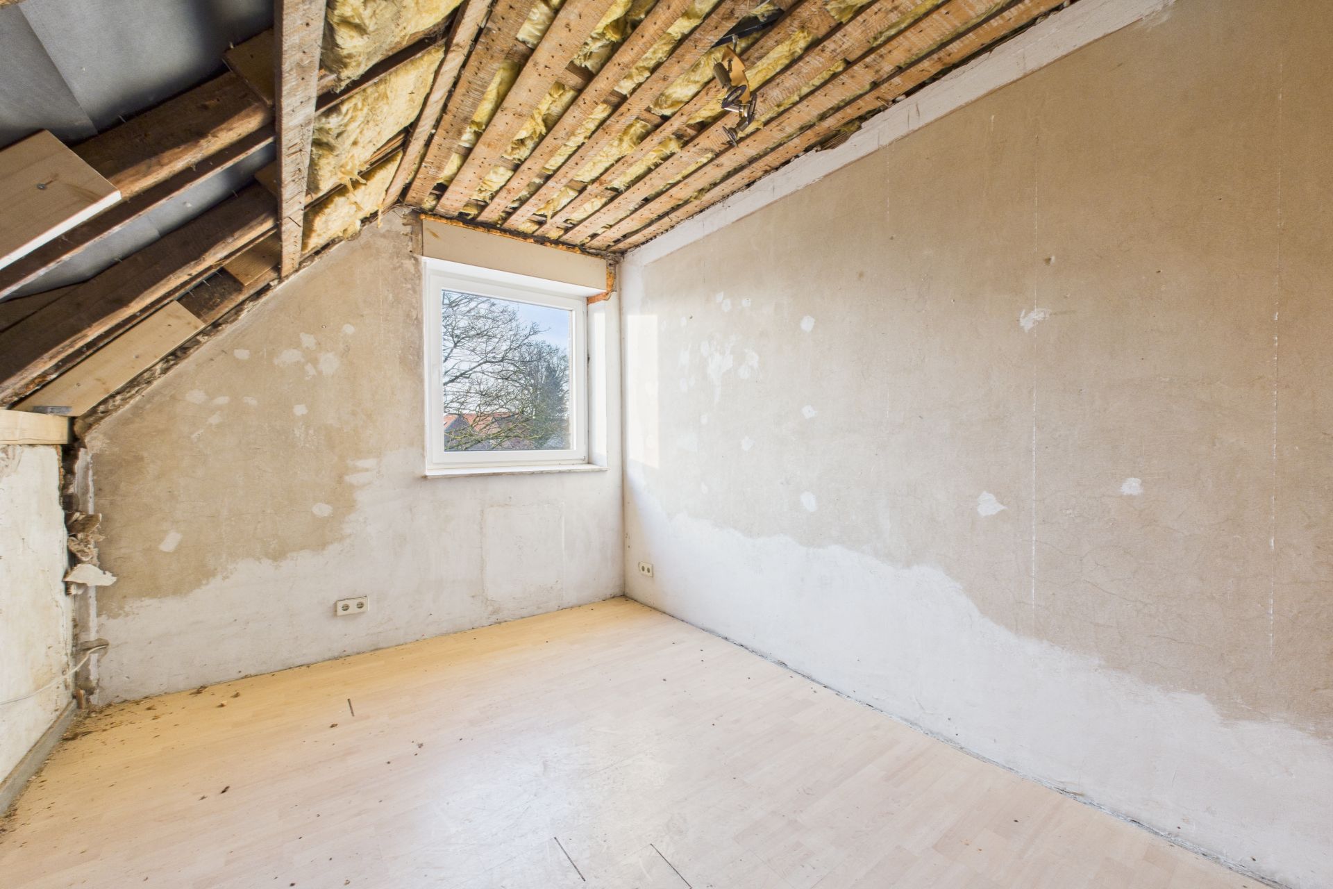 Leerer Dachzimmer mit freiliegender Decke, Fenster und unbehandelten Wänden.