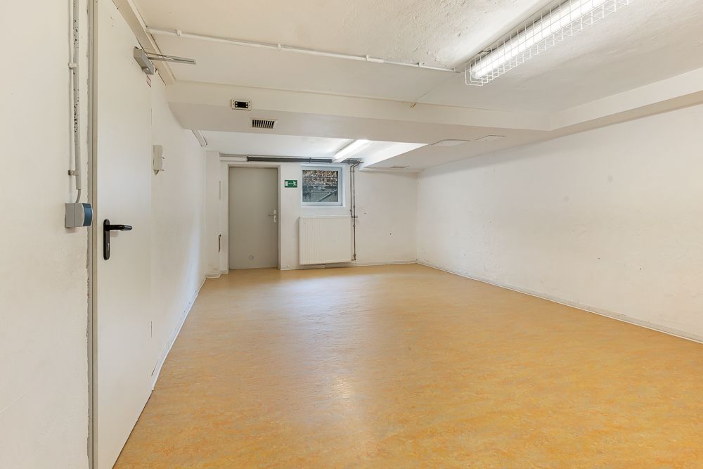 Leerer weißer Kellerraum mit Fenster, Tür und gelbem Bodenbelag.