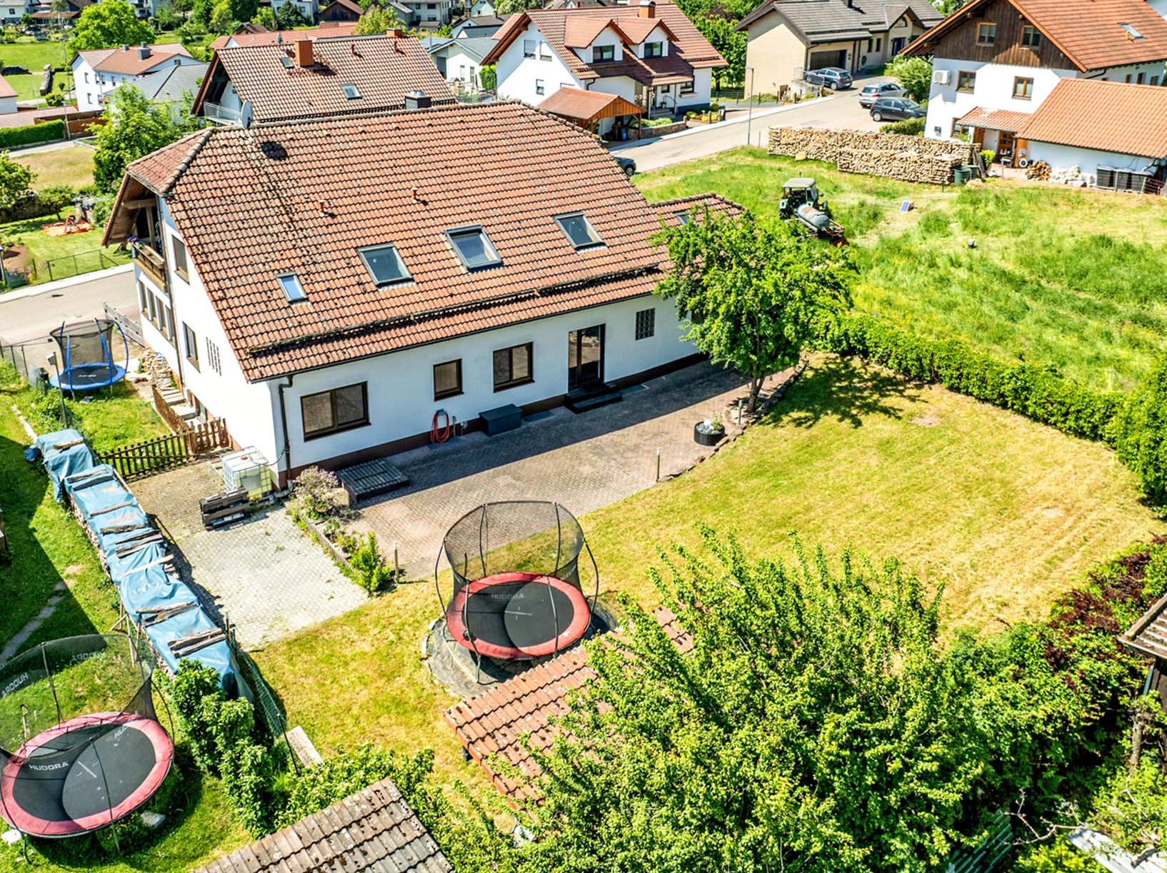 Luftaufnahme eines Wohnhauses mit großem Garten, mehreren Trampolinen und Terrasse.