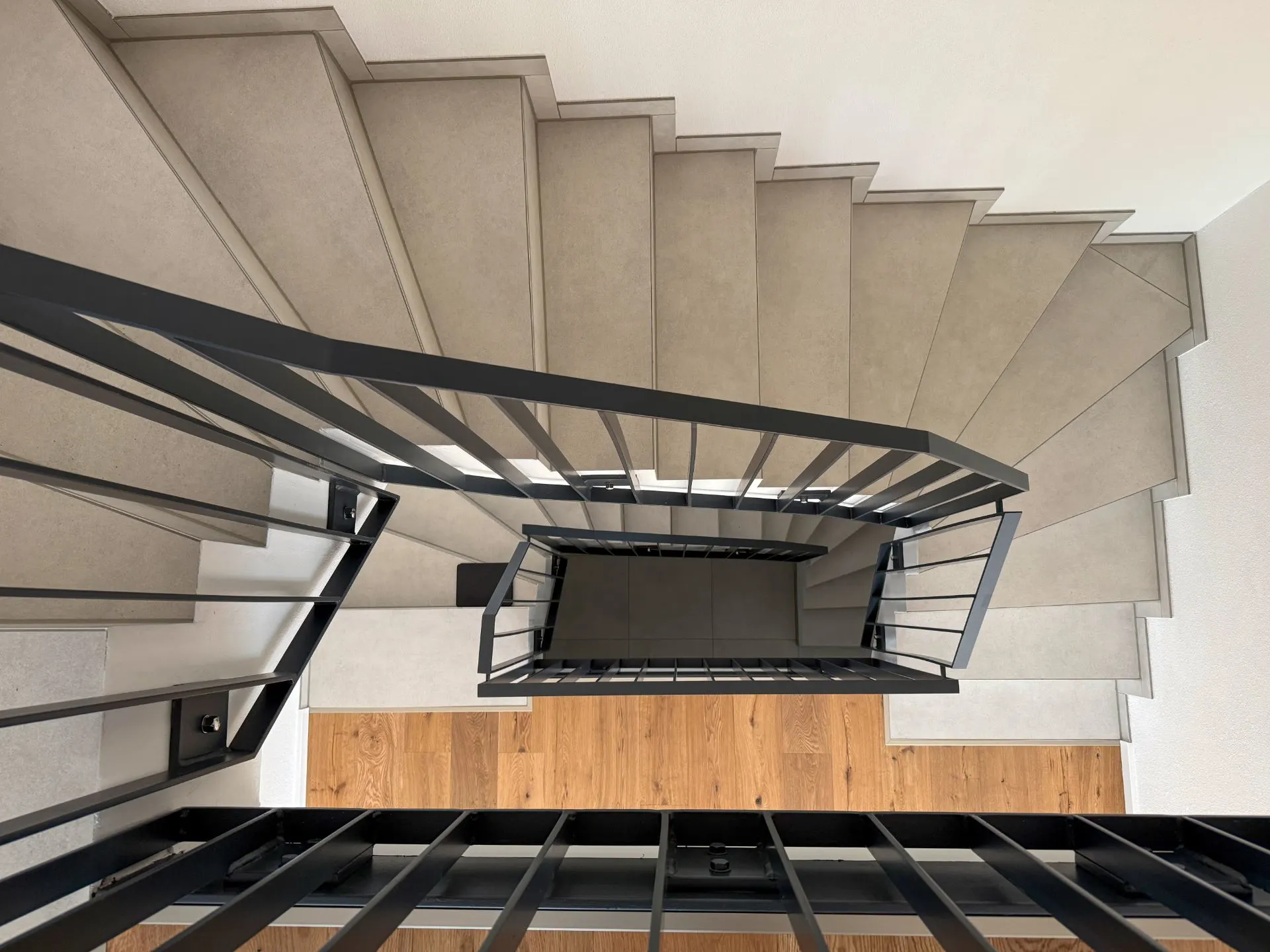 Blick von oben auf eine moderne Treppe mit grauen Stufen und schwarzem Geländer.
