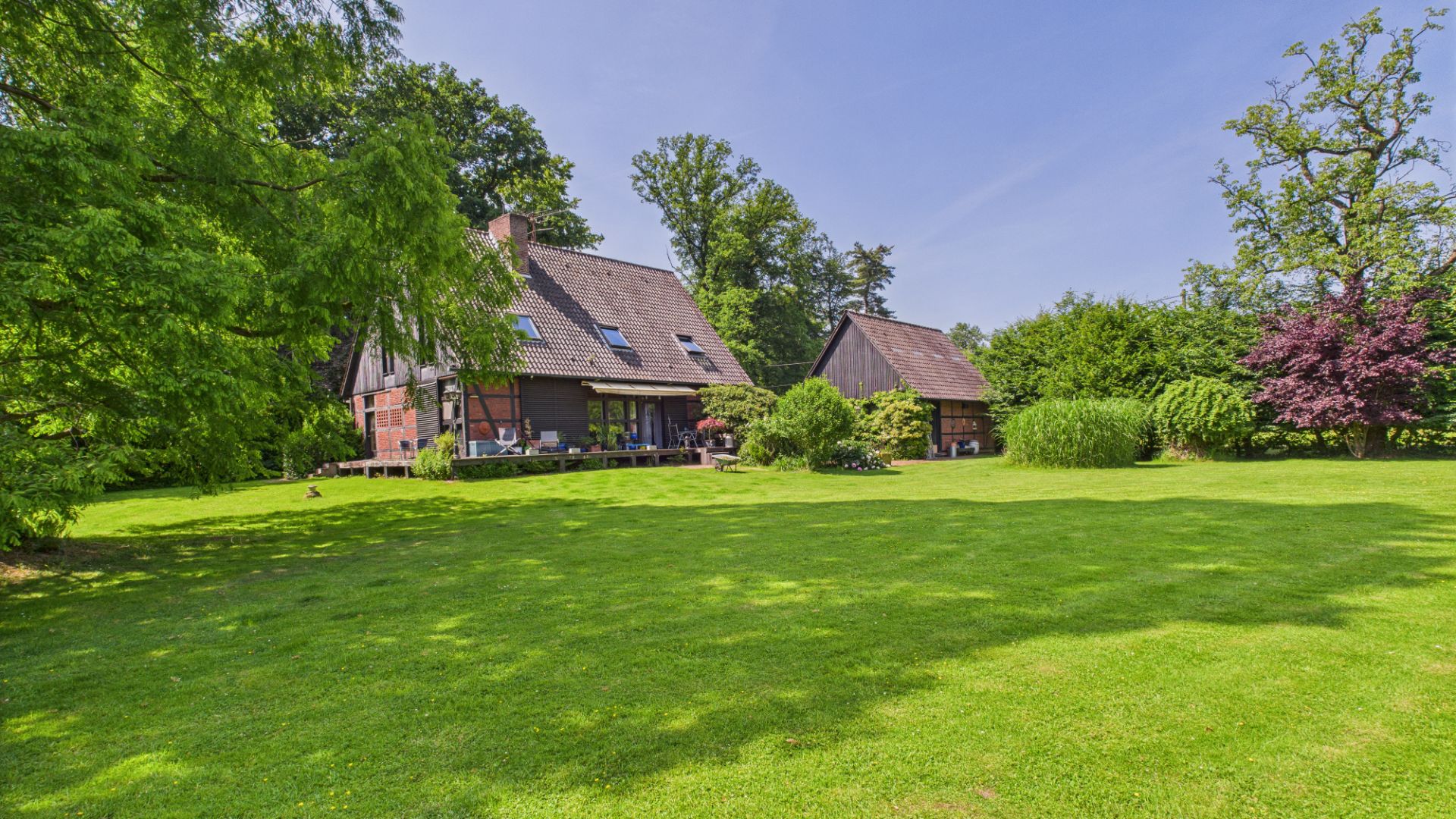 Großes Haus mit Garten, Rasenfläche und Bäumen an einem sonnigen Tag.