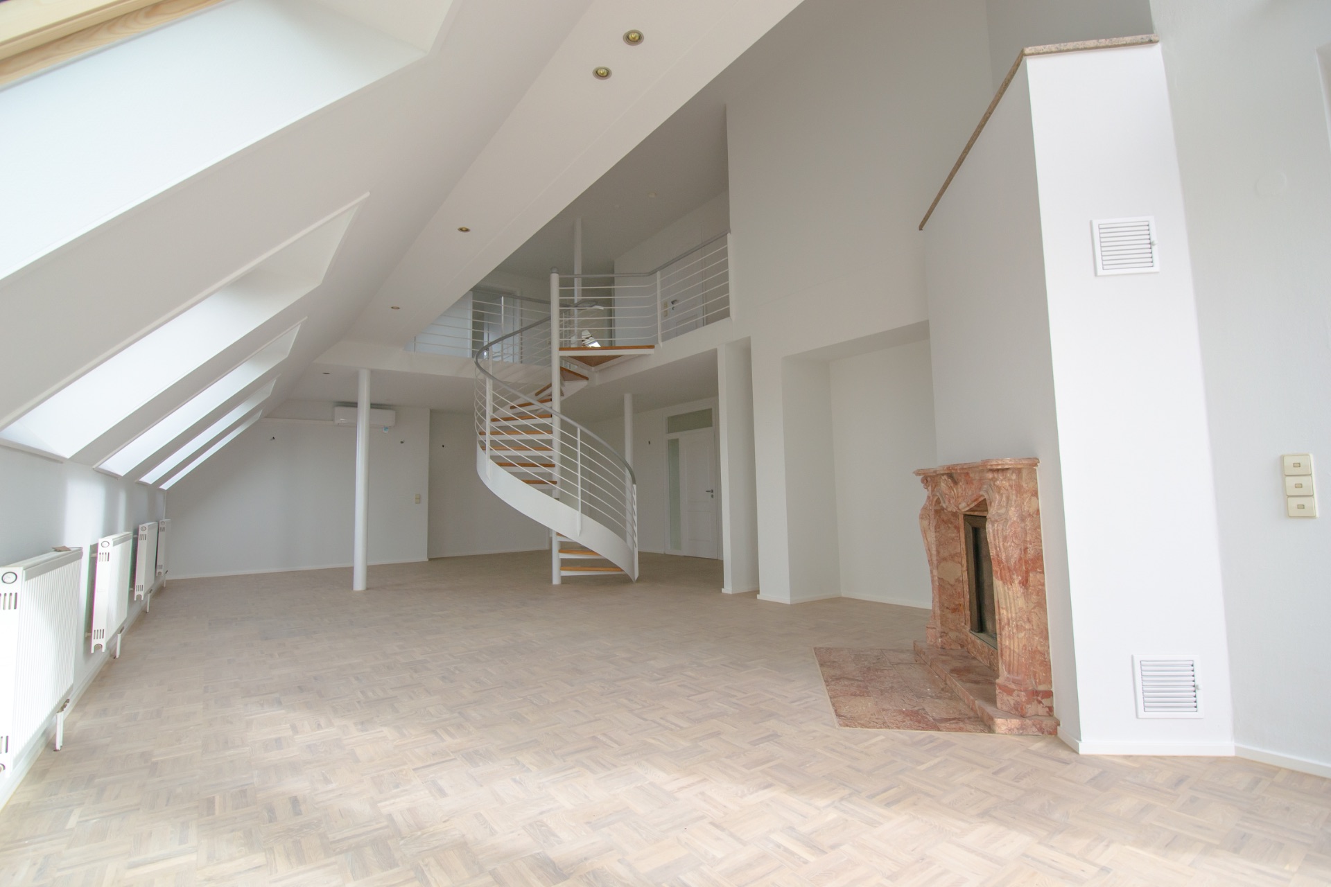 Heller Wohnraum mit Holzfußboden, Kamin und weißer Wendeltreppe im Hintergrund.