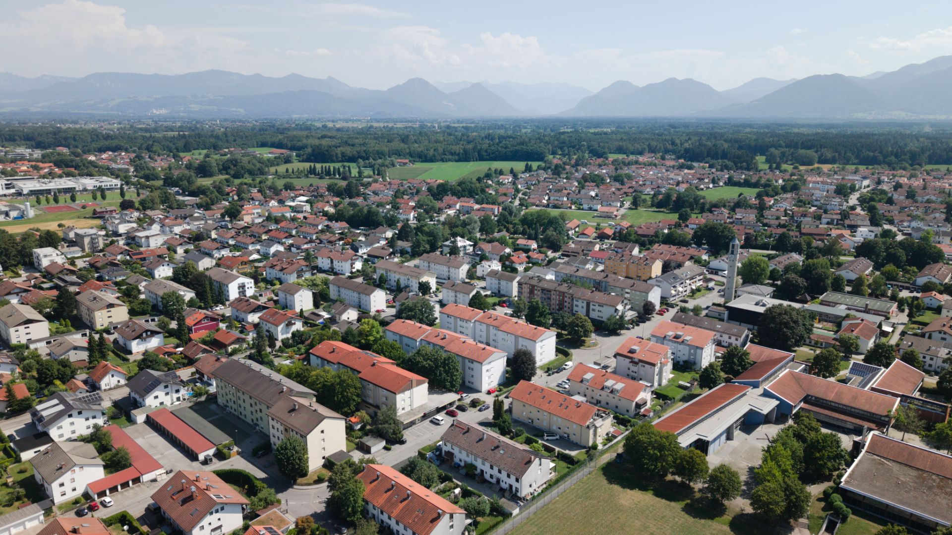 Luftaufnahme einer Wohnsiedlung mit roten Dächern und Bergen im Hintergrund.