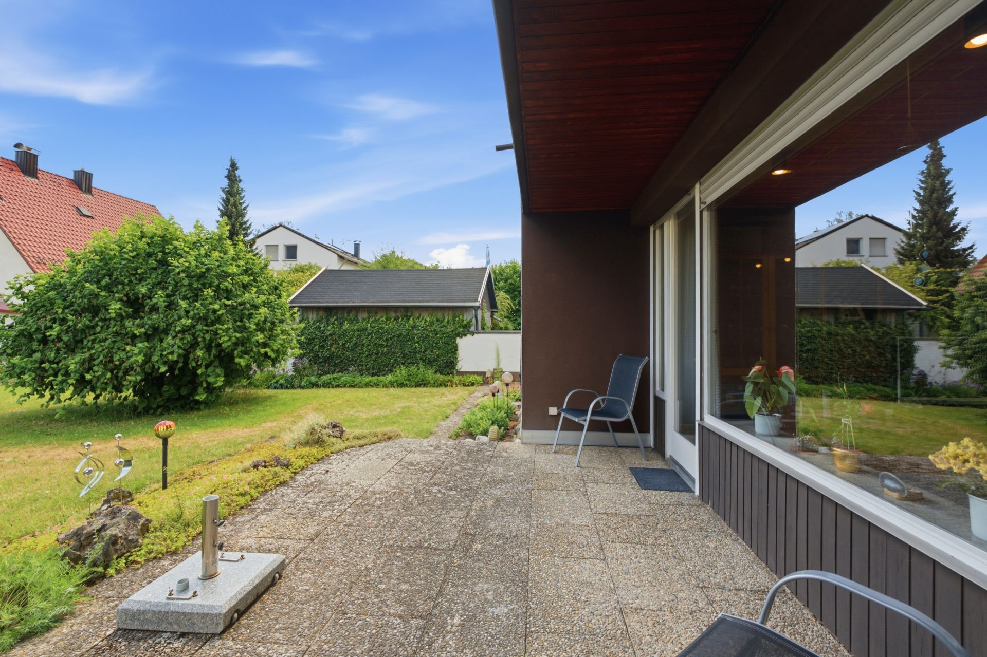 Terrasse mit Stühlen und Blick auf einen grünen Garten, daneben große Fensterfront.