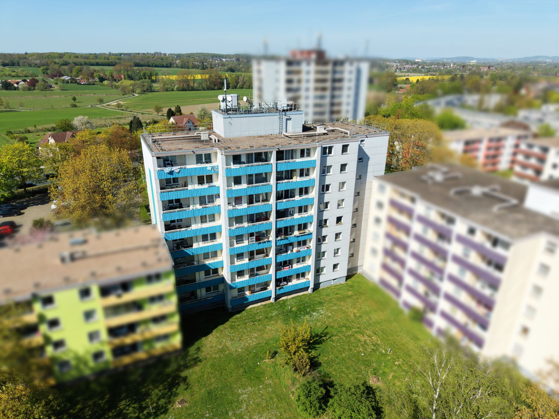 Mehrstöckiges Wohnhaus mit blauen Balkonen, umgeben von weiteren Wohngebäuden und viel Grün.