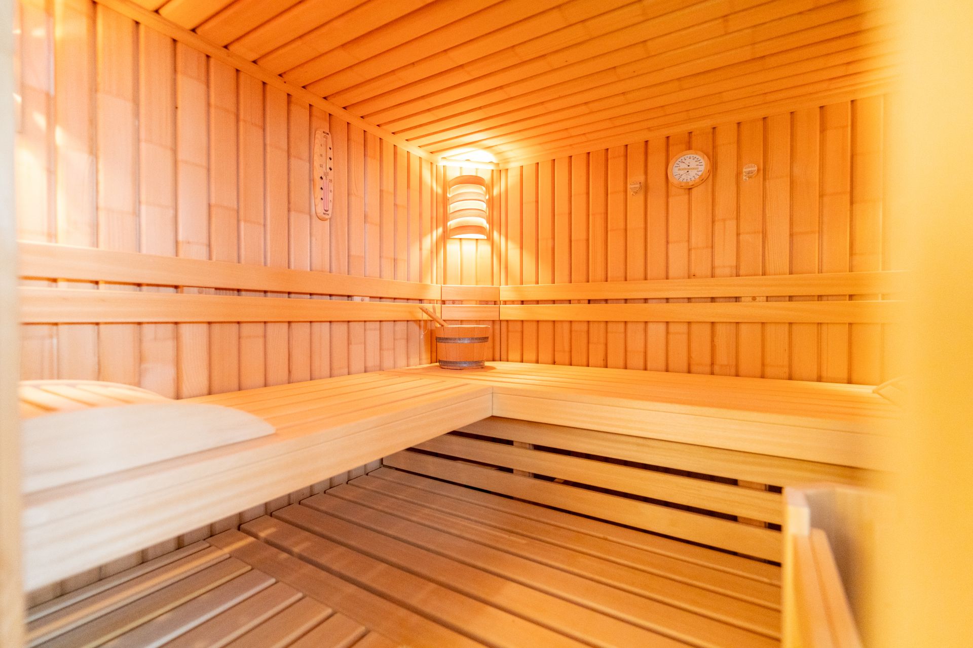 Helle Holzsauna mit Bank, Lampe und Thermometer an der Wand.