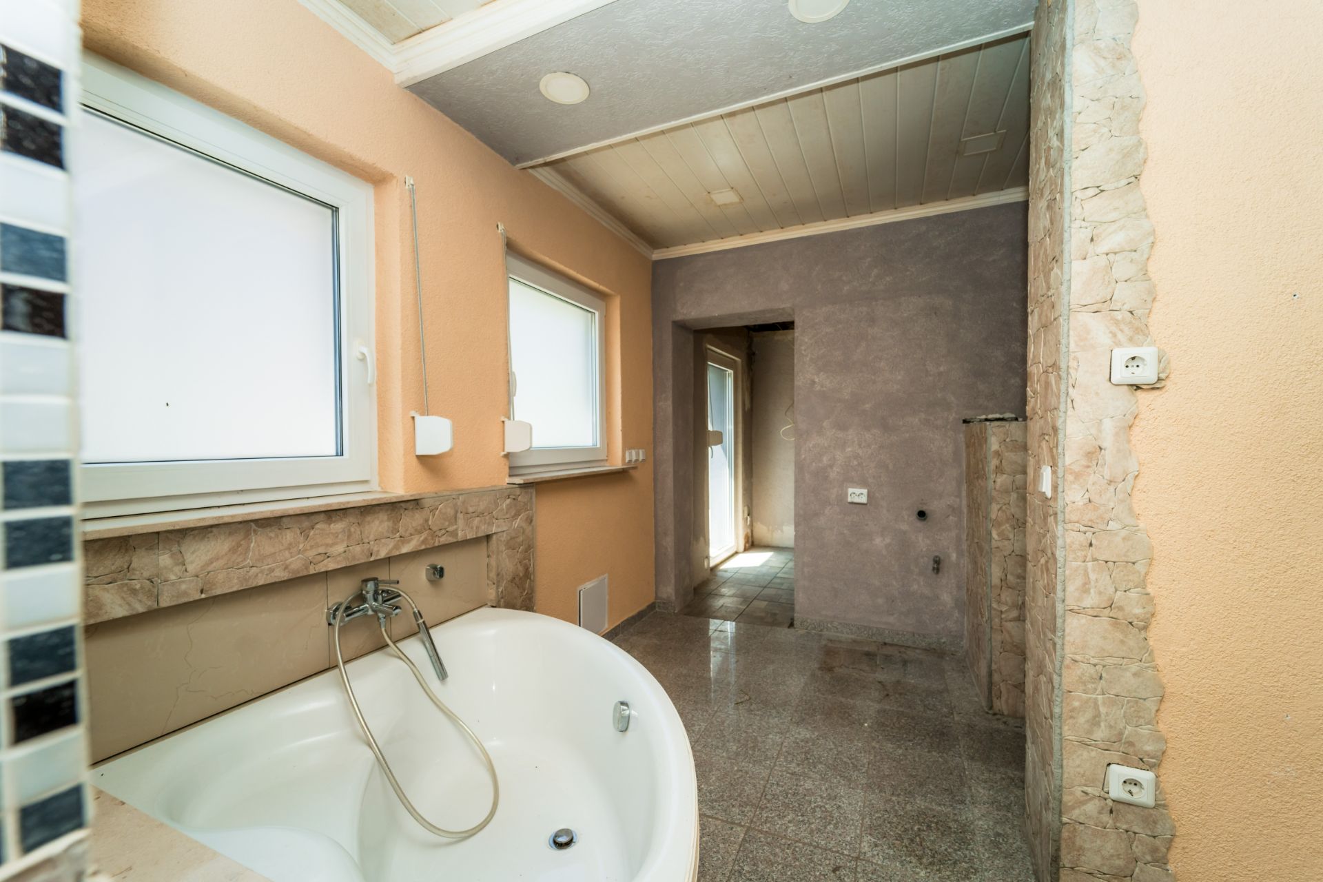 Badezimmer mit runder Badewanne, zwei Fenstern und Fliesenboden, teilweise renoviert.