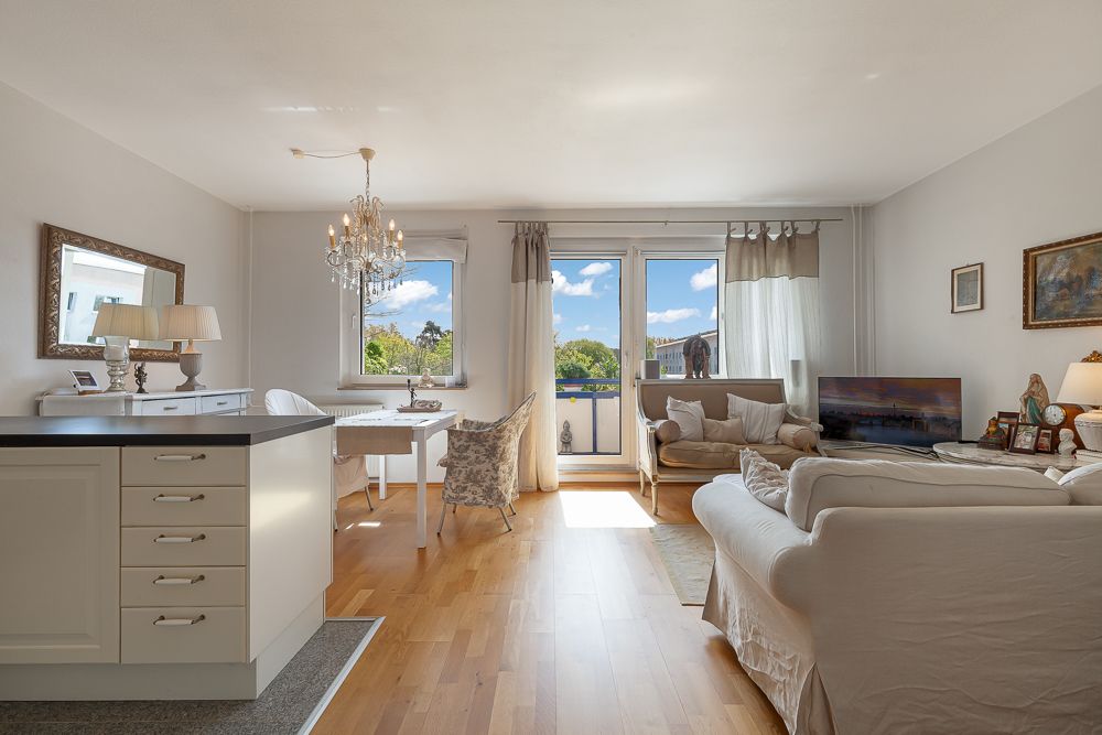 Helles Wohnzimmer mit Sofa, Essbereich, Kronleuchter und Zugang zum Balkon.