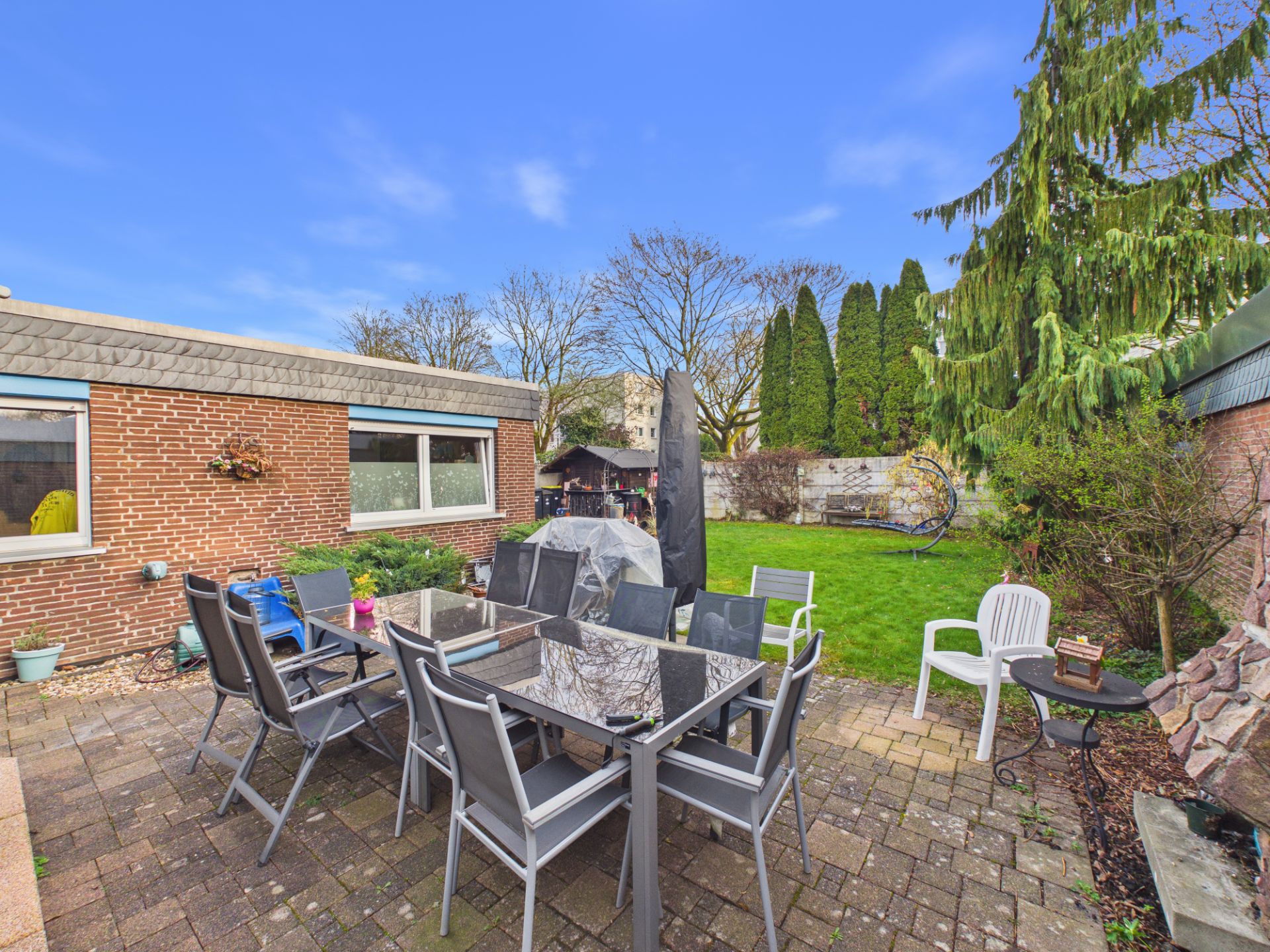 Garten mit Terrasse, Esstisch, Stühlen und Grill neben einem Backsteinhaus.