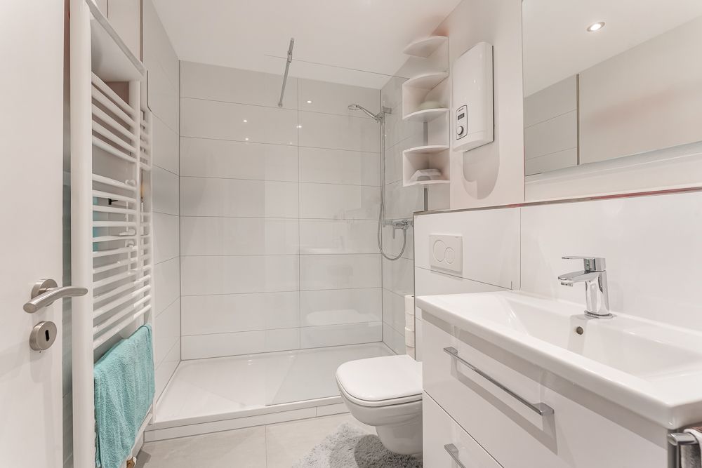 Modernes, weißes Badezimmer mit Dusche, Waschbecken, Toilette und Handtuchheizkörper.