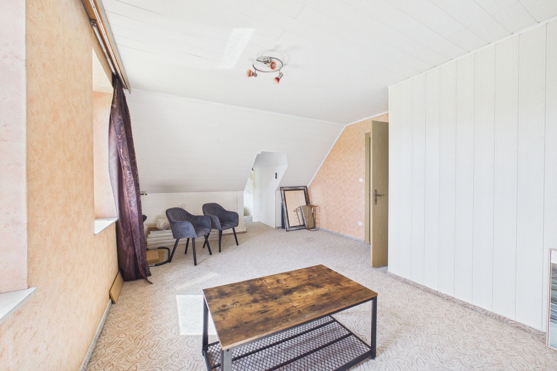 Helles Zimmer mit zwei grauen Stühlen, Holztisch und schräger Decke.
