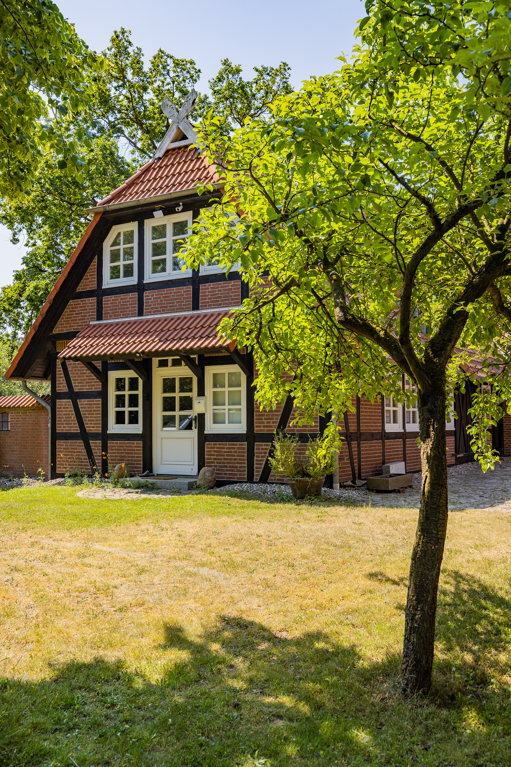 Fachwerkhaus mit rotem Dach, Garten und Baum im Vordergrund.