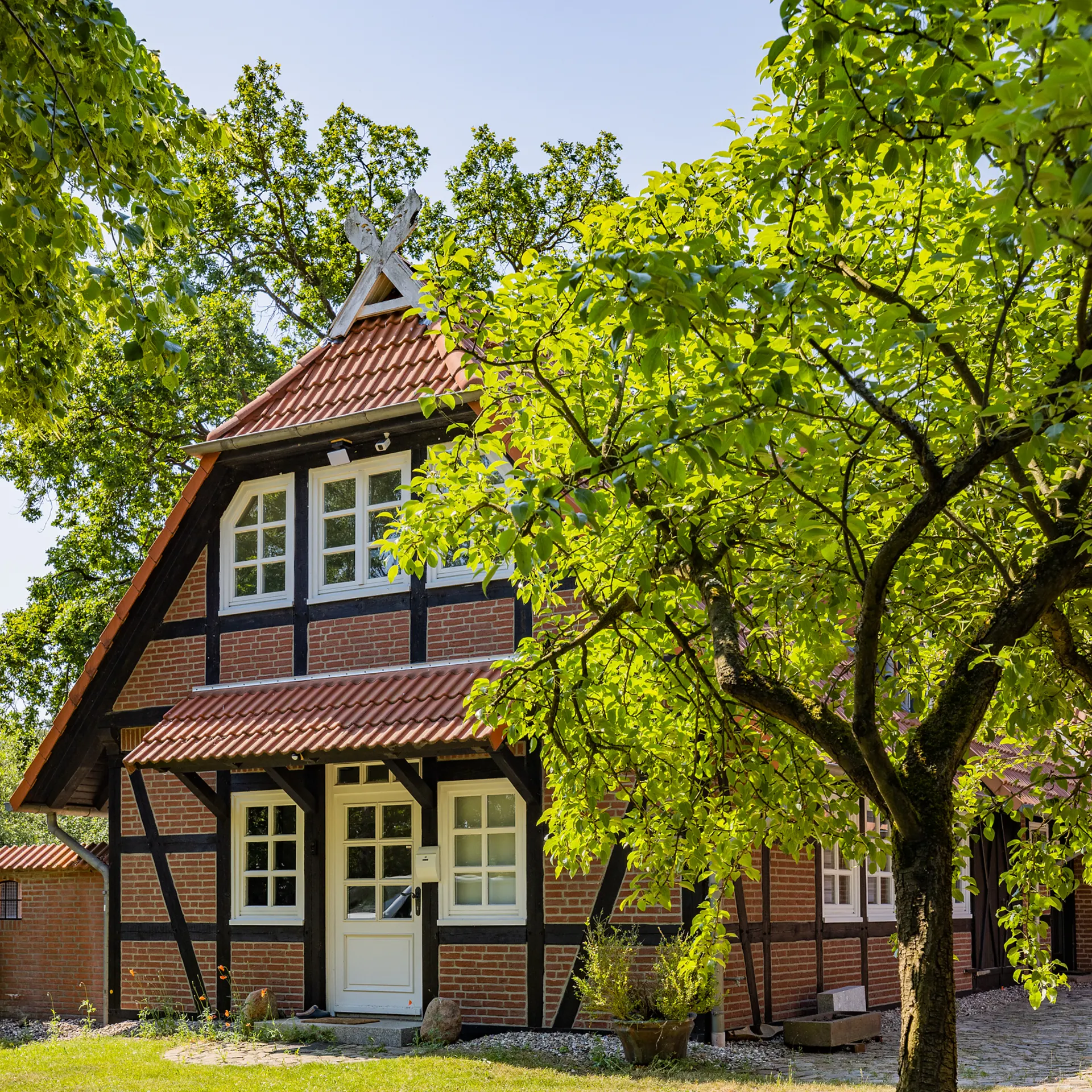Fachwerkhaus mit rotem Dach, Garten und Baum im Vordergrund.