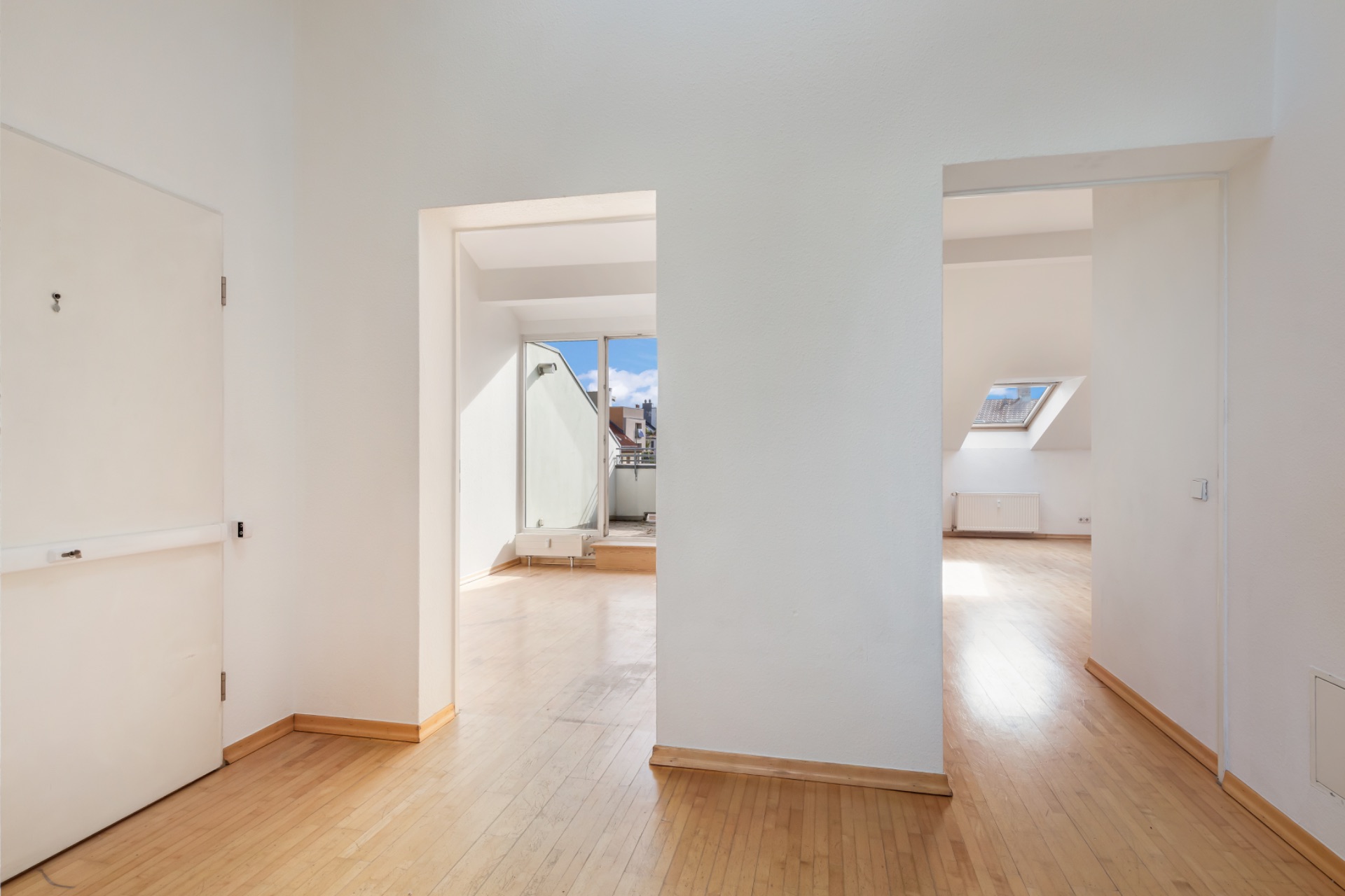 Heller Flur mit Holzboden und zwei offenen Türen zu weiteren Zimmern, Fenster im Hintergrund.
